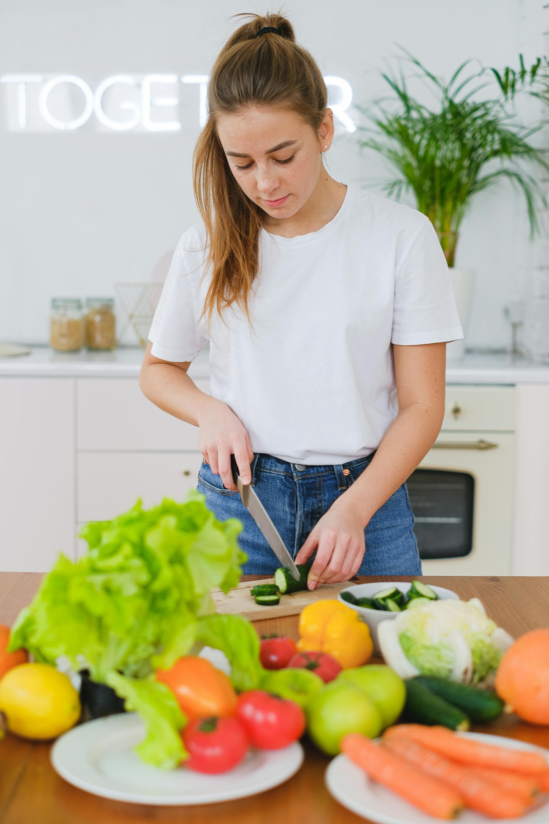 Young woman in white t-shirt slicing vegetables in a modern kitchen setting, focusing on healthy eating.