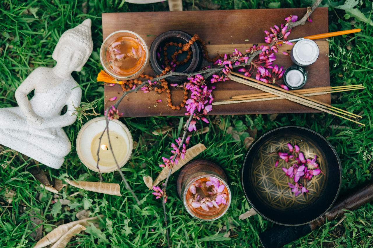 Peaceful outdoor meditation scene with Buddha, flowers, incense, and candles.