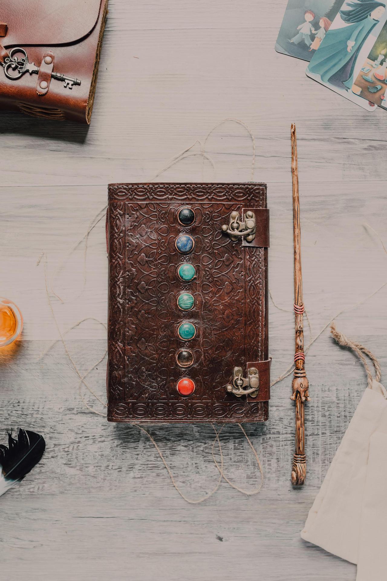 Flat lay of a leather journal with chakra stones, a wand, and mystical elements on a wooden surface.