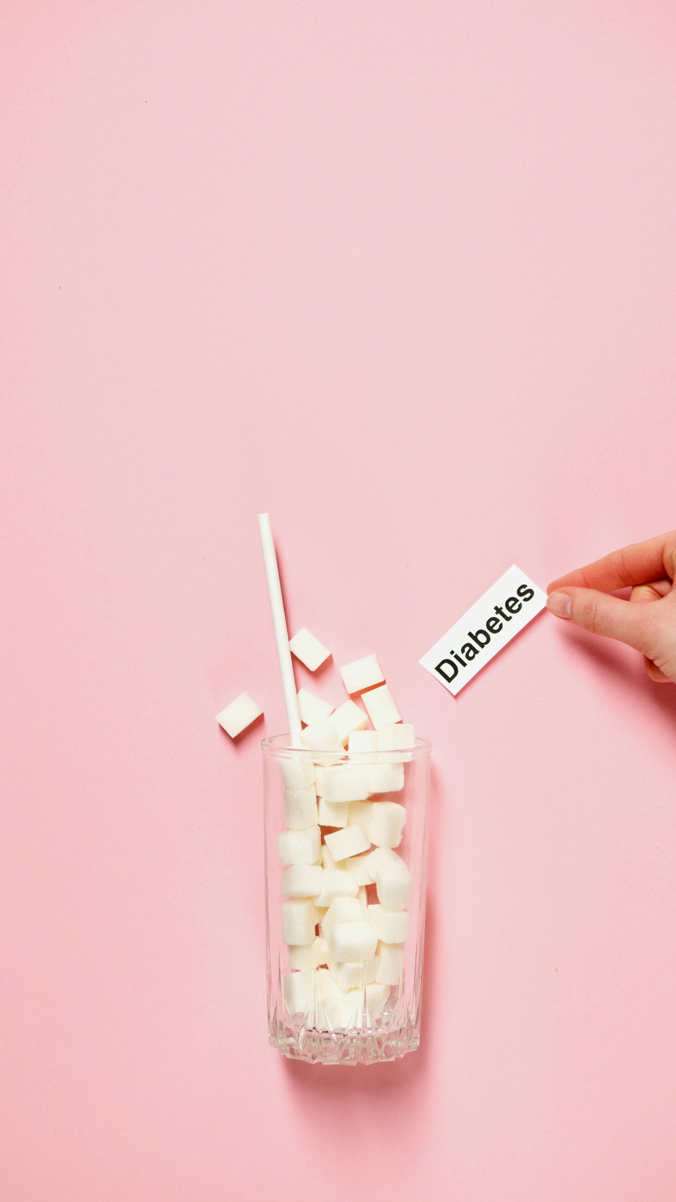Glass of sugar cubes with diabetes label on pink background.