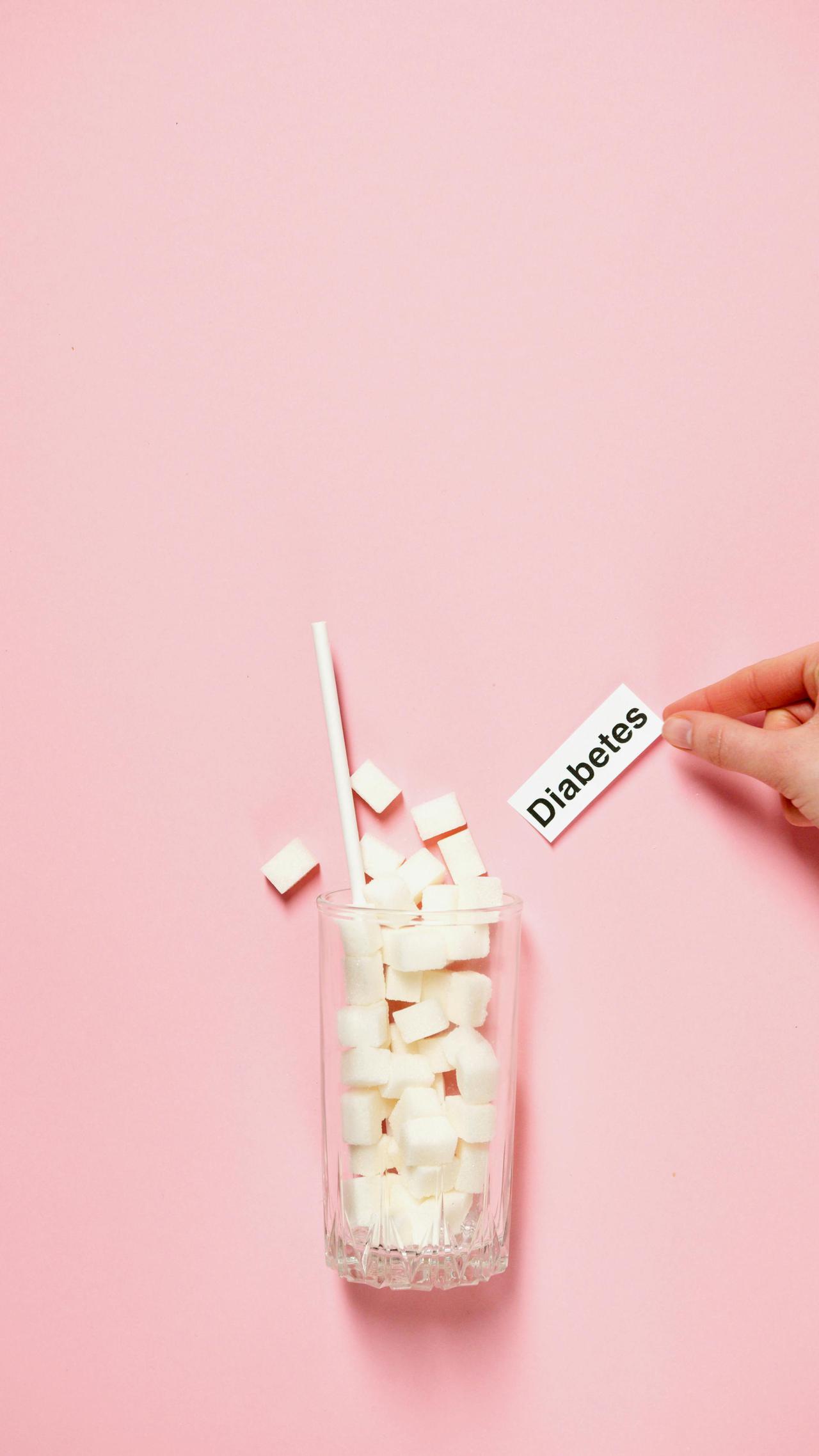 Glass of sugar cubes with diabetes label on pink background.
