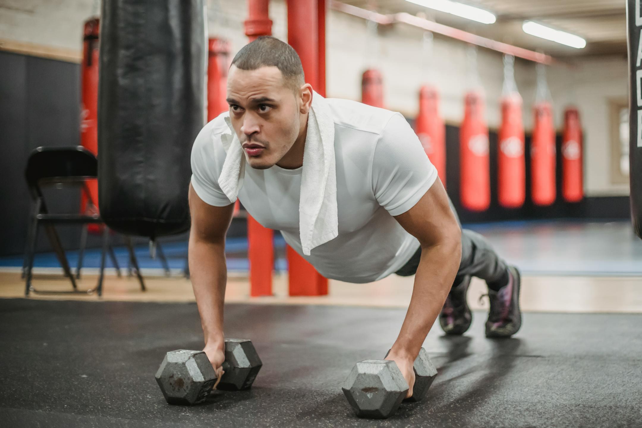 Focused man performing push-ups using dumbbells in a gym setting, showcasing strength and determination.