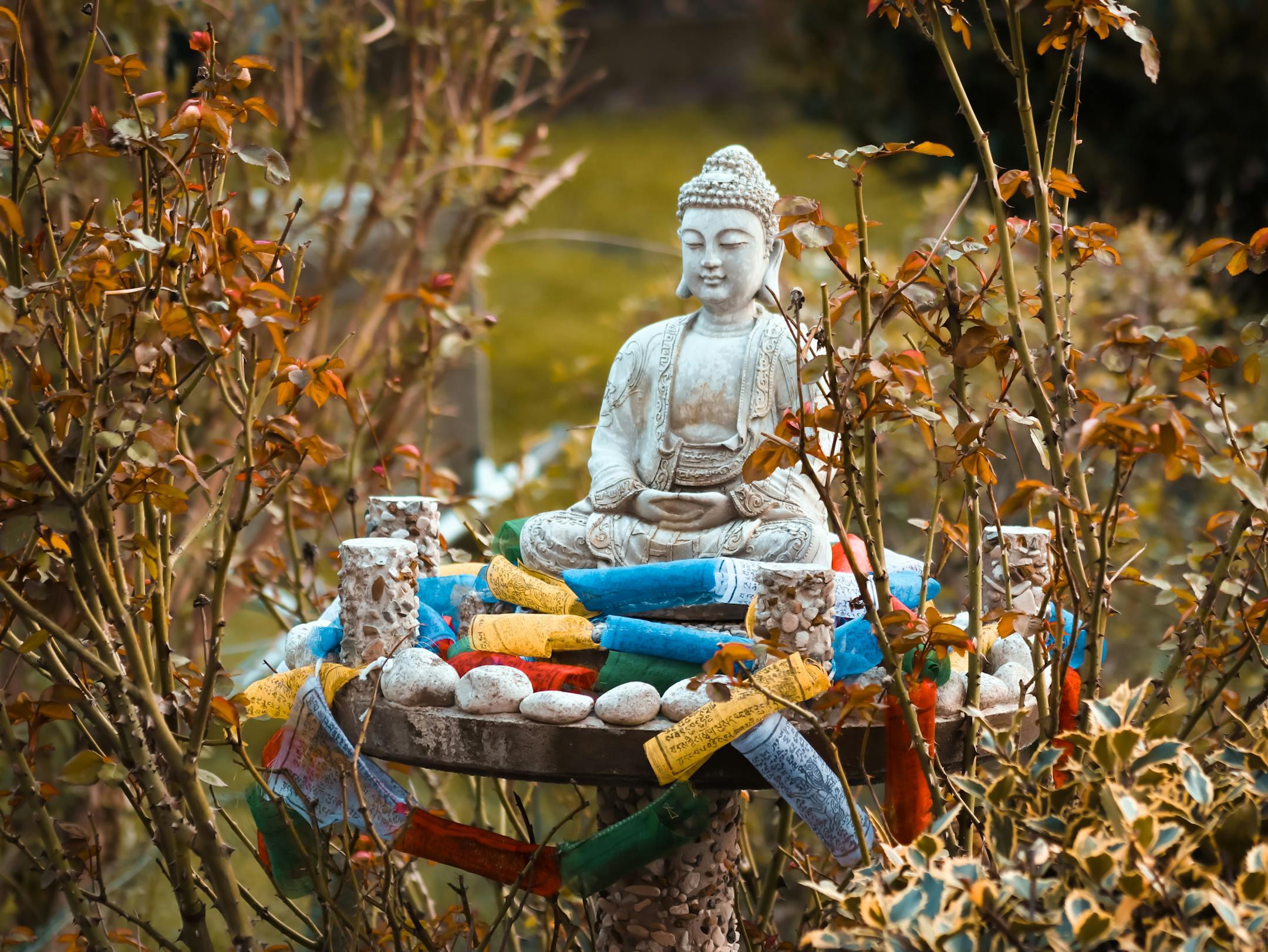 Buddha statue surrounded by colorful prayer flags in a tranquil outdoor setting, embodying peace and spirituality.