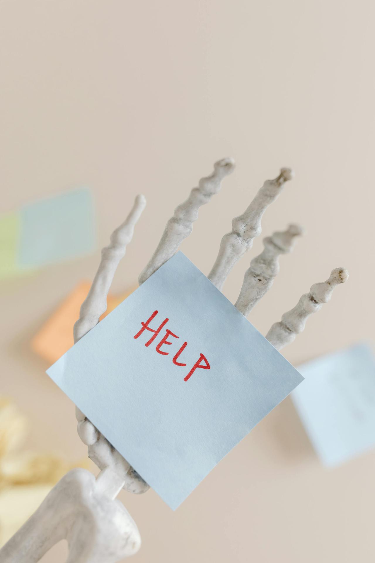 Skeleton hand holding a note with 'HELP' written, symbolizing burnout and stress.