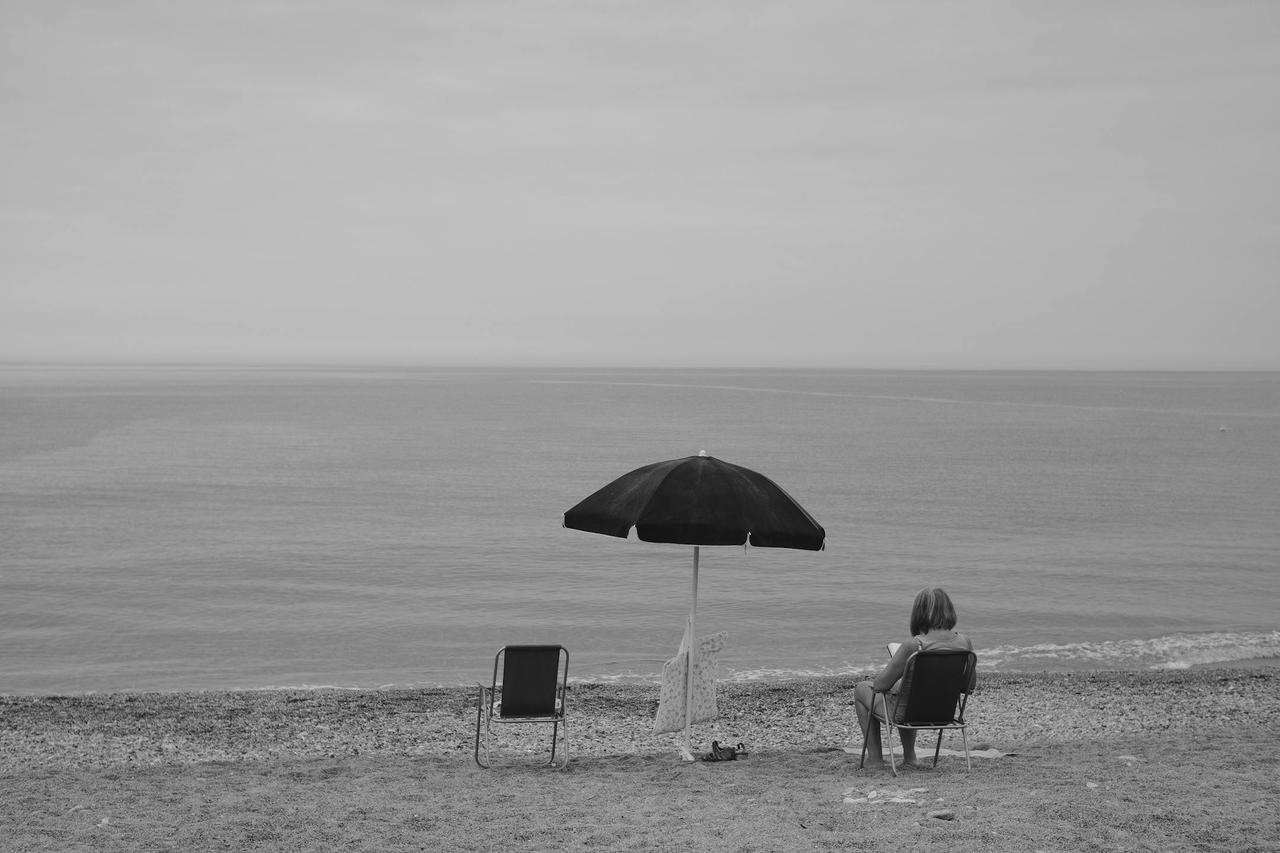 Serene black and white beach scene with a lone woman under an umbrella in Italy.