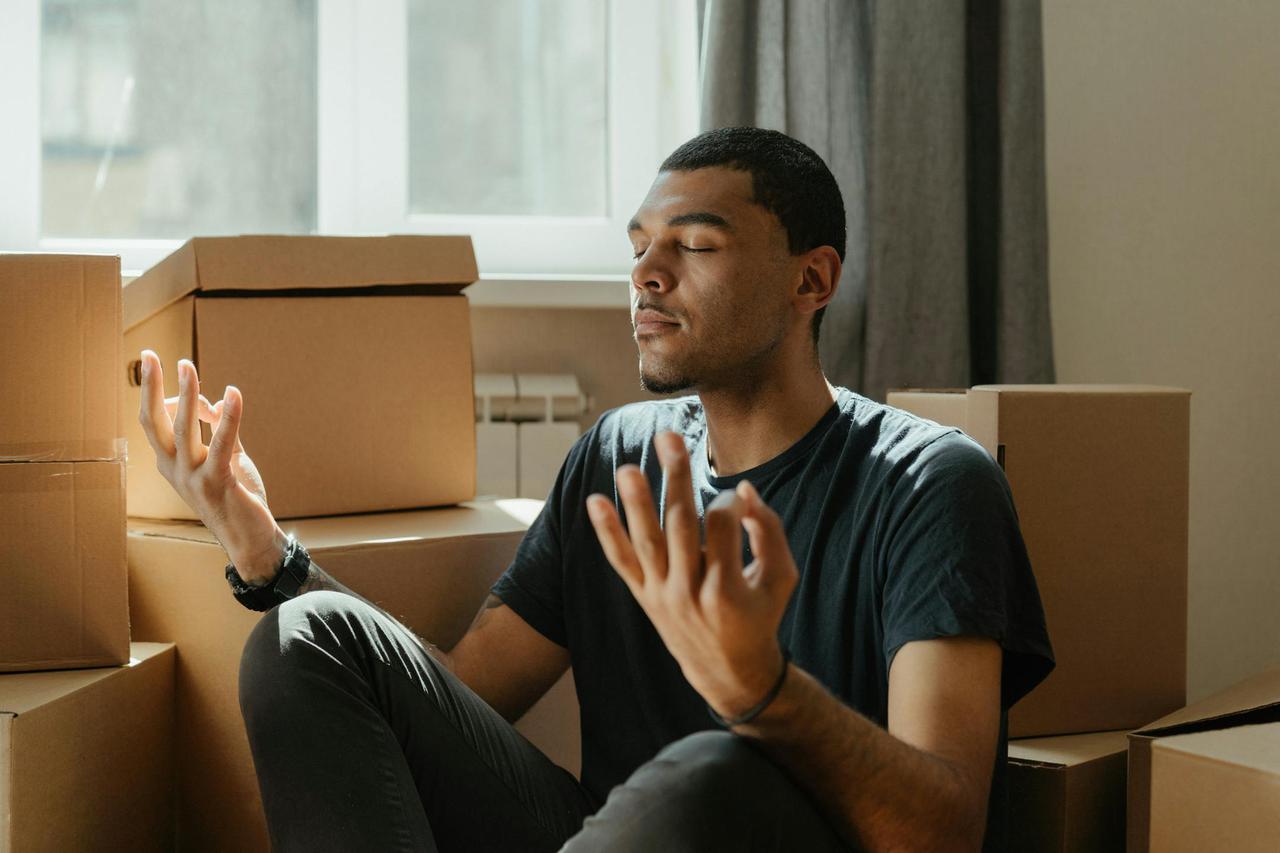 A young man practices meditation surrounded by cardboard boxes during a move.