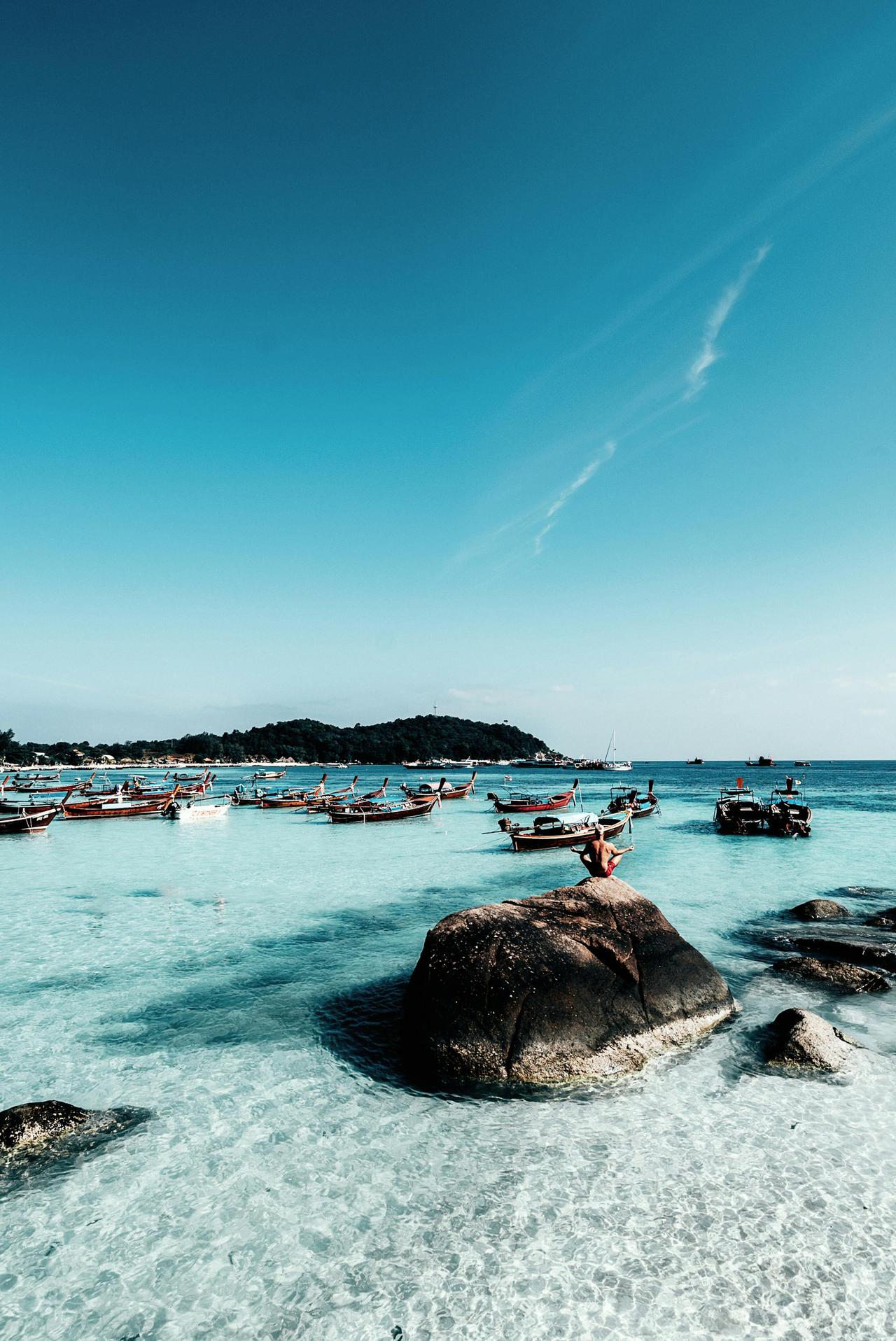 Explore the crystal-clear waters and scenic beauty of Koh Lipe, Thailand, with traditional boats dotting the coastline.