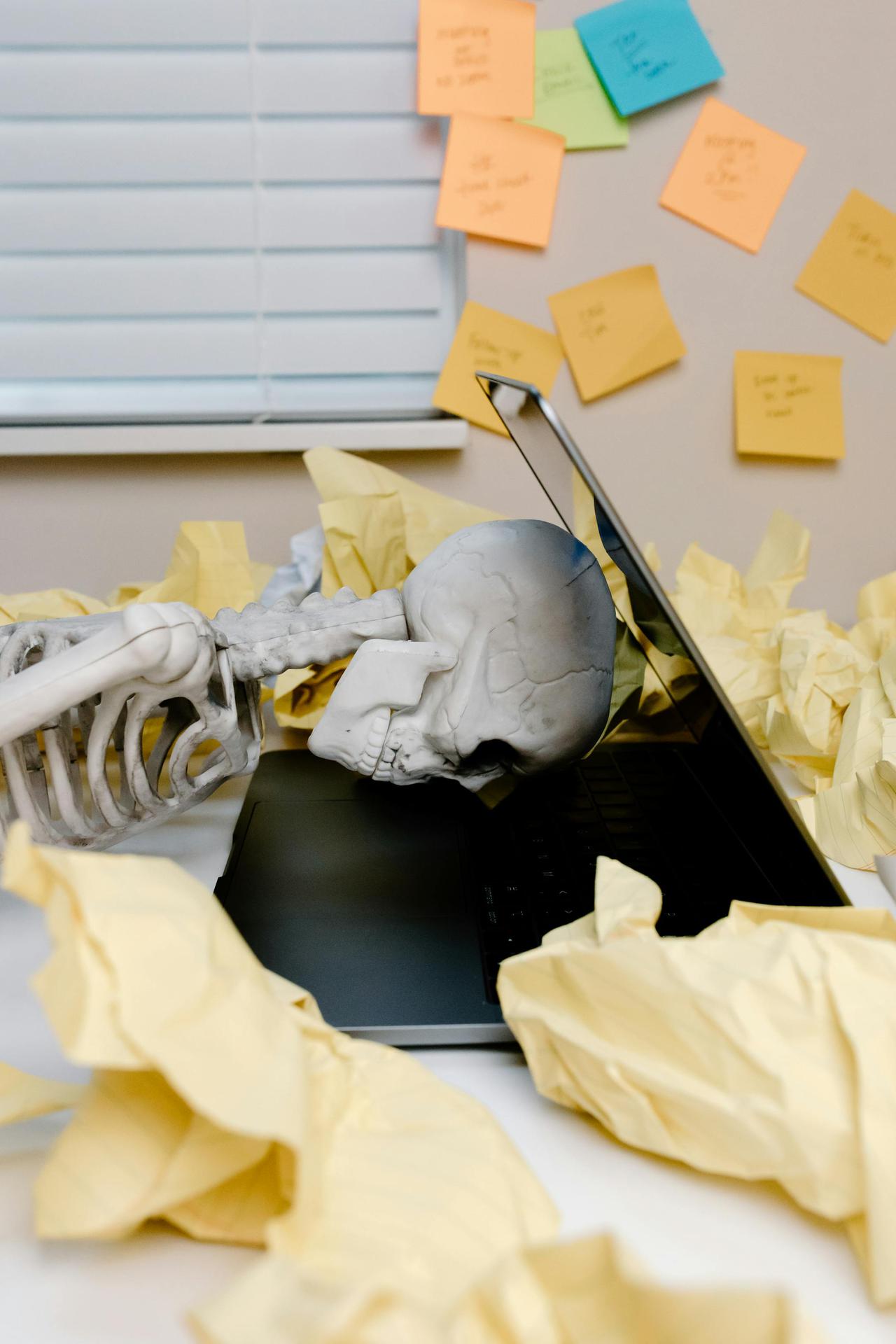 Humorous scene of skeleton at laptop, highlighting work burnout and fatigue.