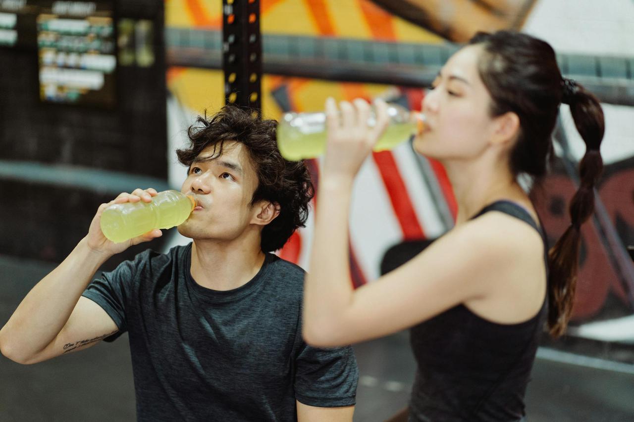 Fit Asian couple hydrating at the gym after an intense workout. Refreshing drink break.