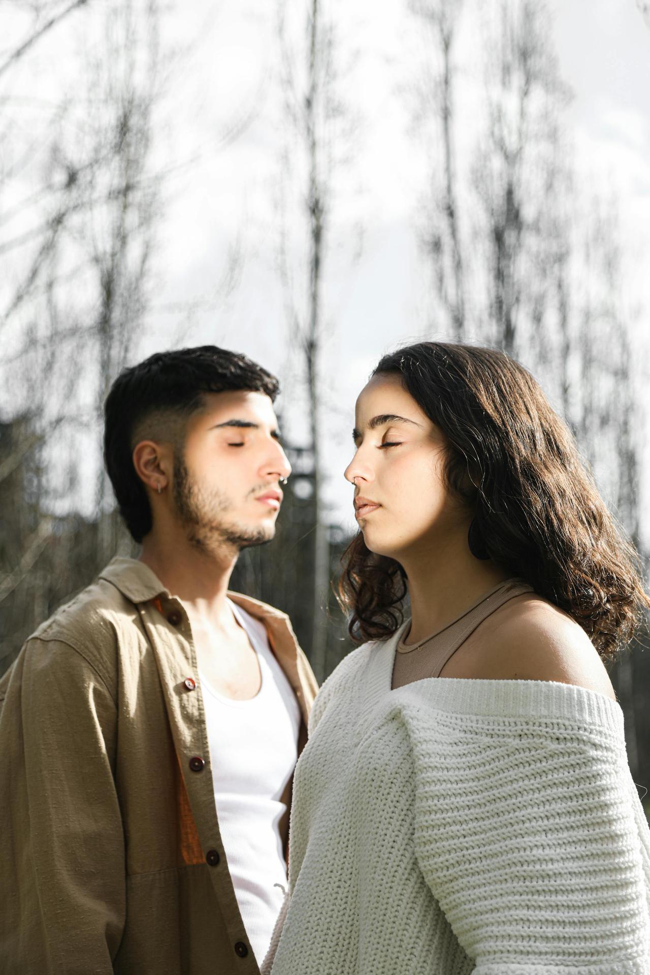 Serene couple with eyes closed meditating outdoors among trees, reflecting peace and harmony.