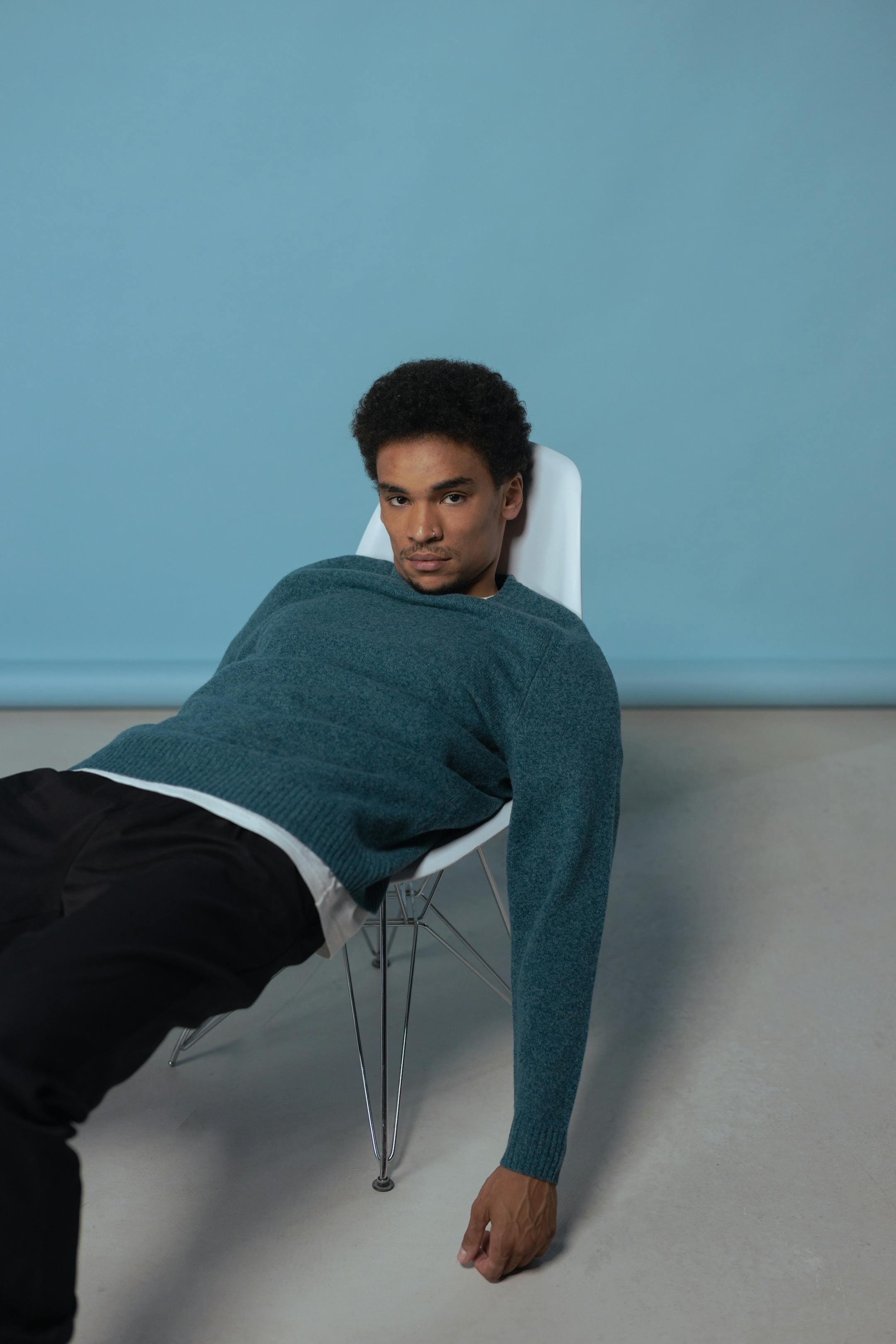 Stylish man with afro hair lounging on a chair in a modern studio setting.