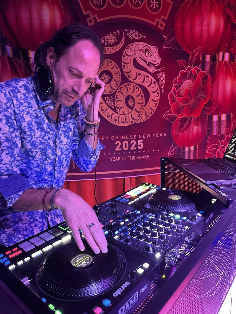 Professional DJ mixing music at an event with colorful lights and dancing guests.