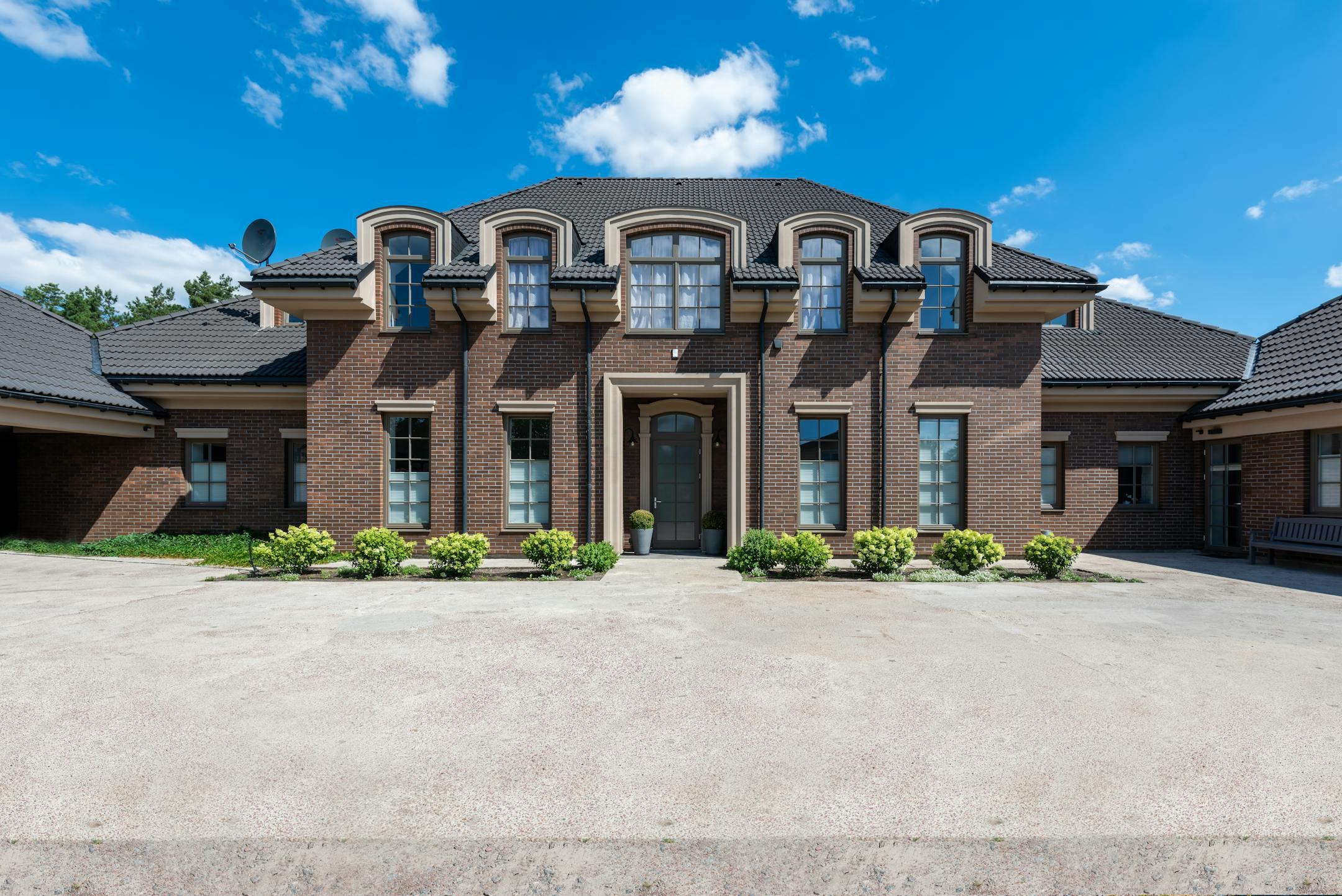 Elegant two-story brick house exterior with classic architecture under a bright blue sky.