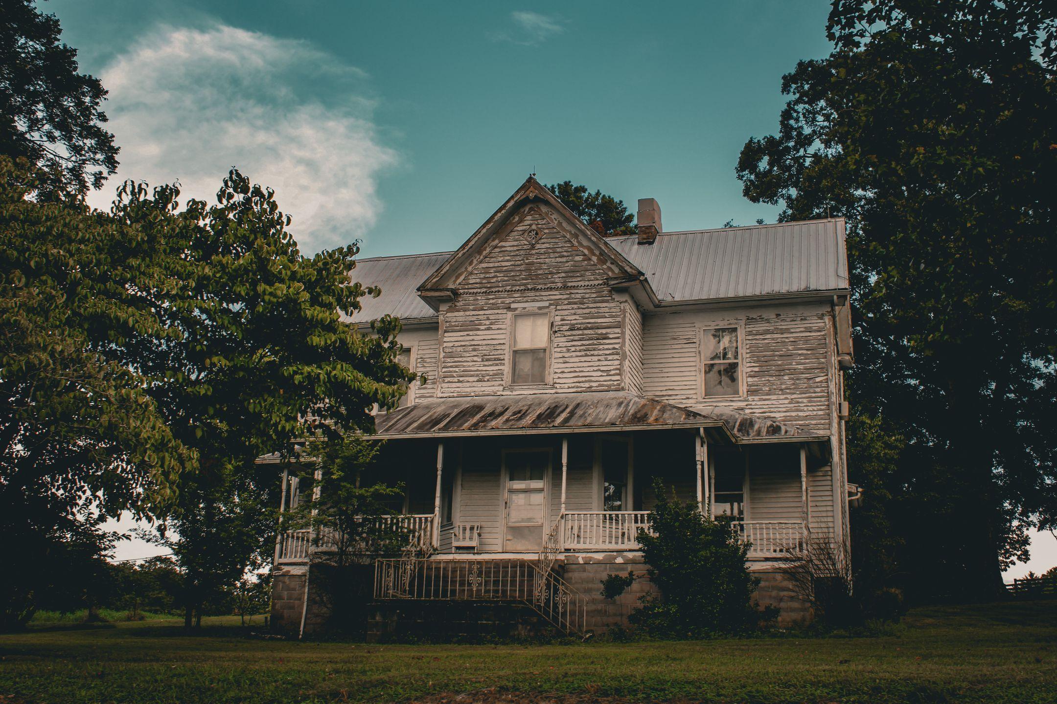 Rustic abandoned Victorian house surrounded by trees, embodying timeless architecture and mystery.