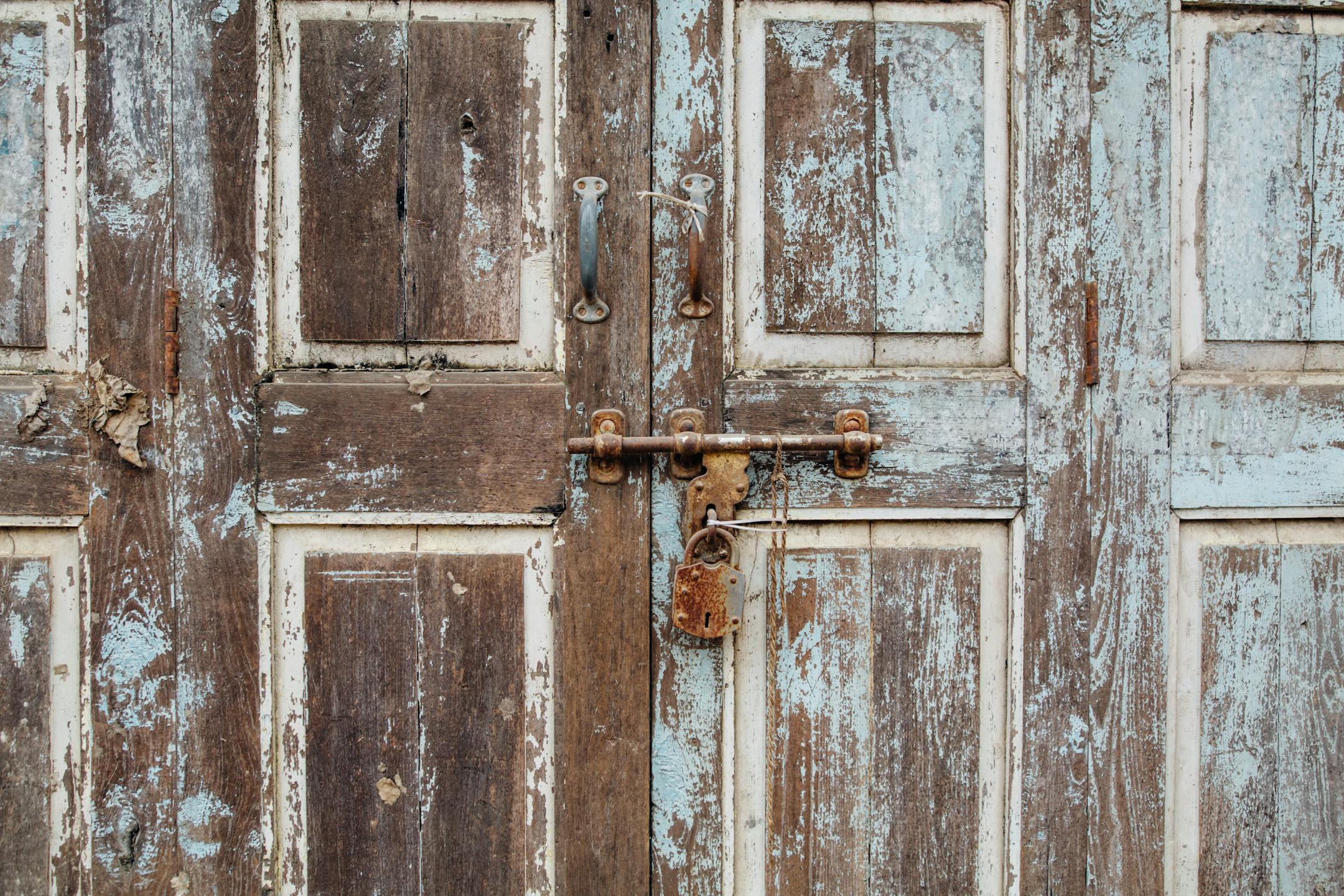 Close-up of an old wooden door with a rusty padlock, showcasing decay and texture.