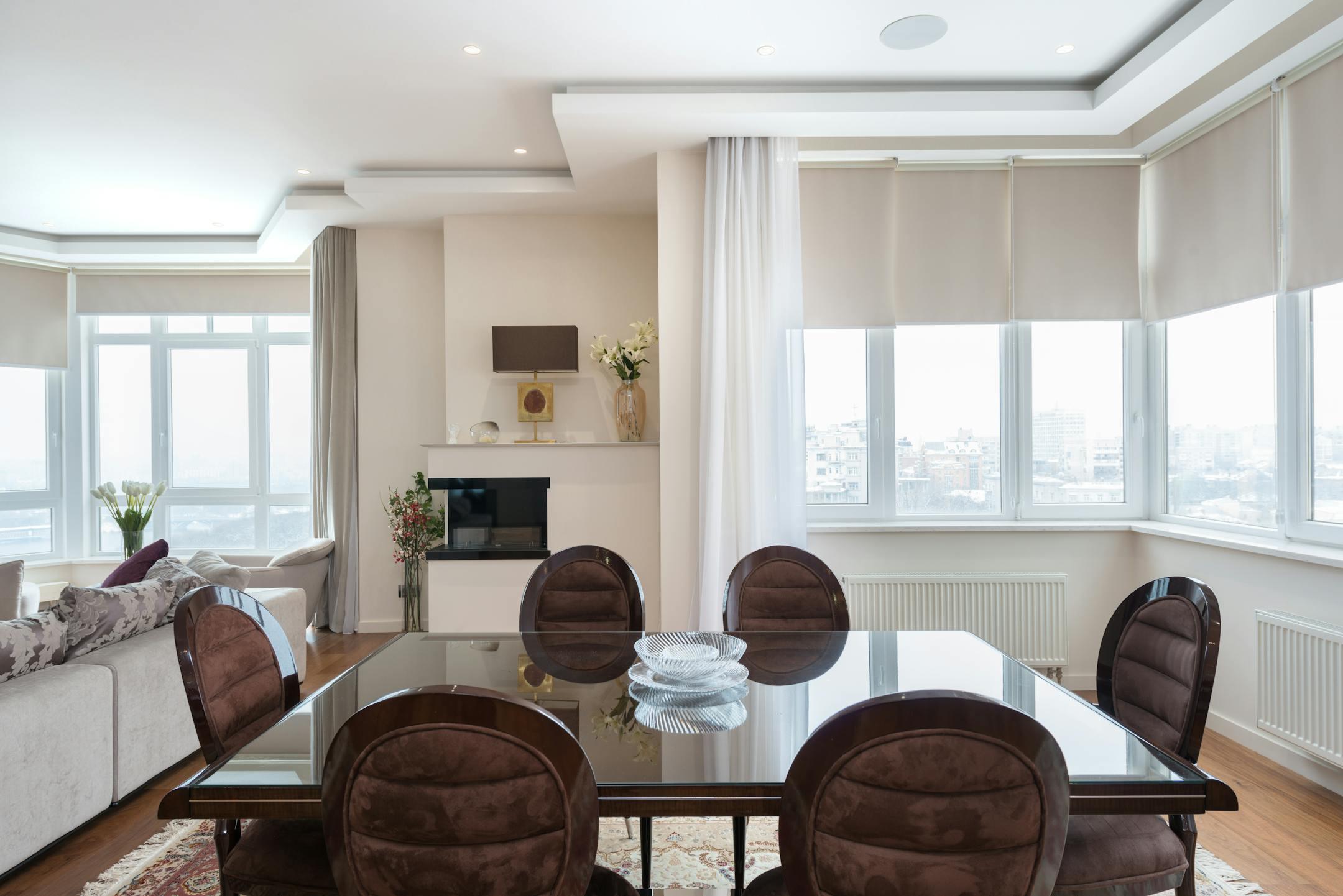 Classic styled wooden dining table with soft chairs placed near windows in spacious living room with cozy sofa in daylight