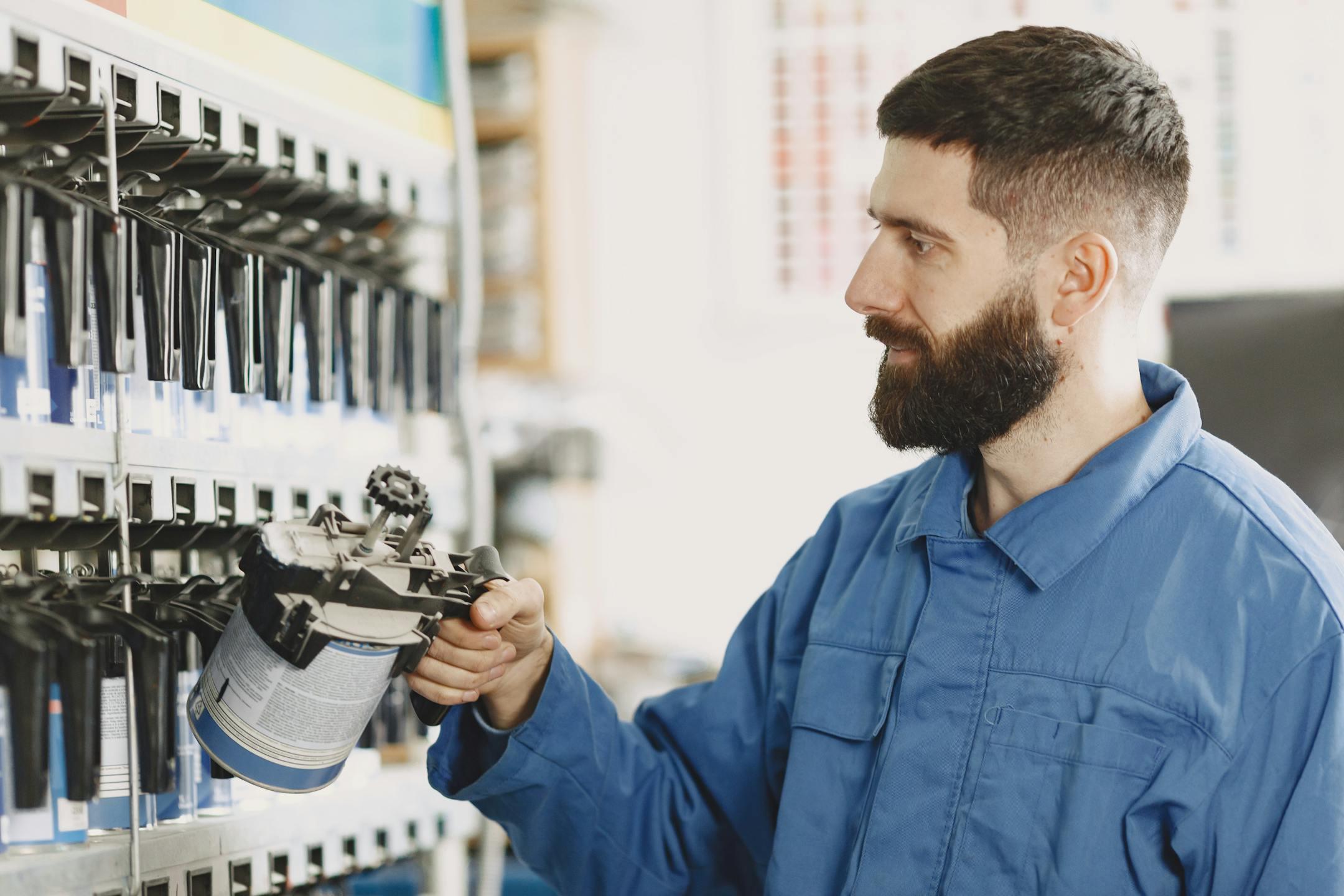 Bearded automobile mechanic selecting spray paint in a well-organized workshop with various tools.