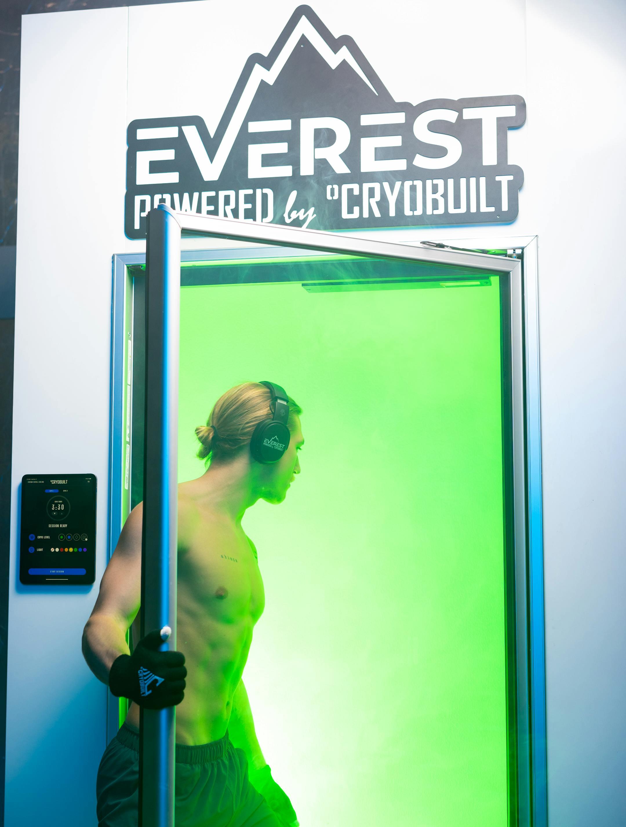 A man exits a futuristic cryotherapy chamber, showcasing advanced fitness technology.