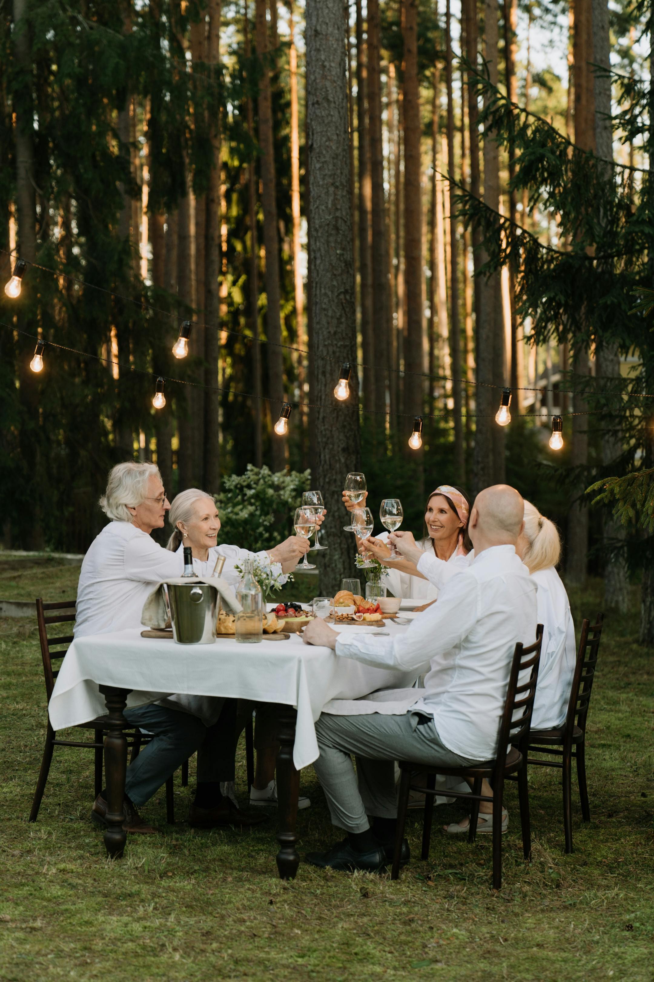 A group of friends toasting in a cheerful outdoor dinner setting surrounded by nature.