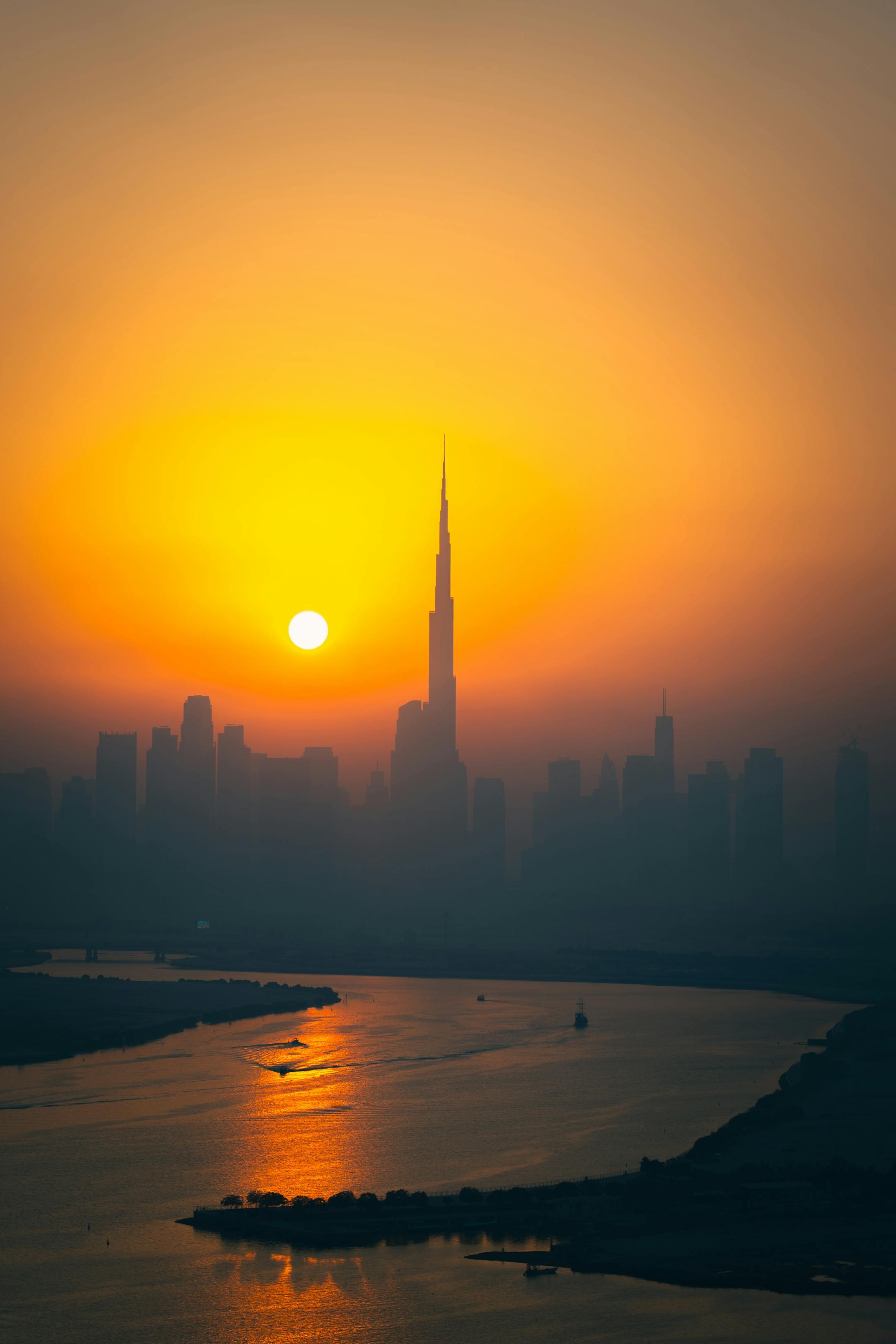 A breathtaking view of Dubai skyline with the iconic Burj Khalifa at sunset, reflecting over the water.