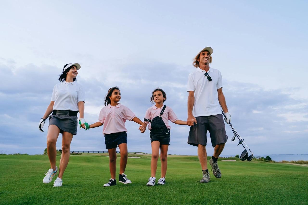 Happy family walking on a golf course together, enjoying leisure time outdoors with golf clubs.