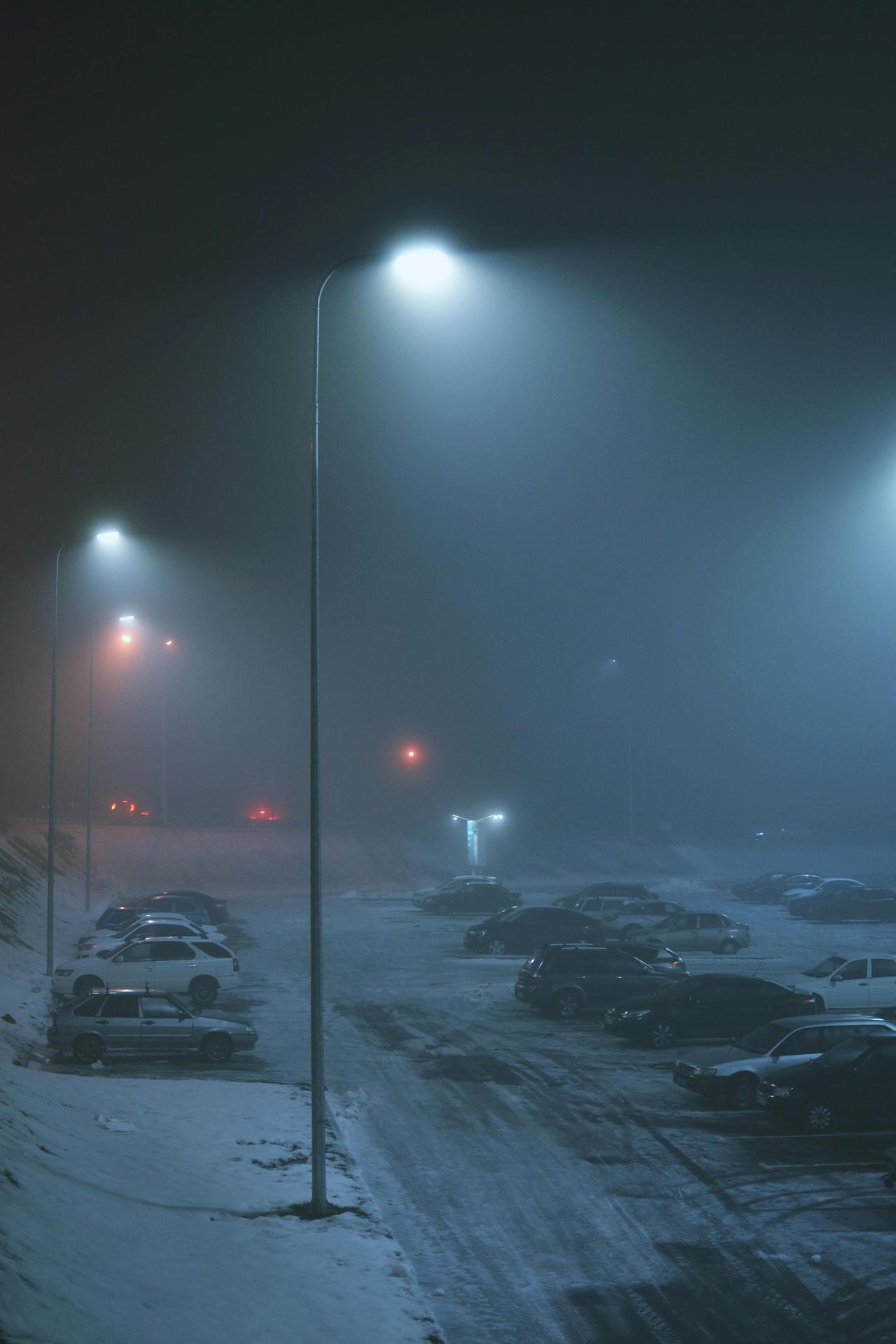 Snow-covered parking lot in winter, illuminated by street lights on a misty night.