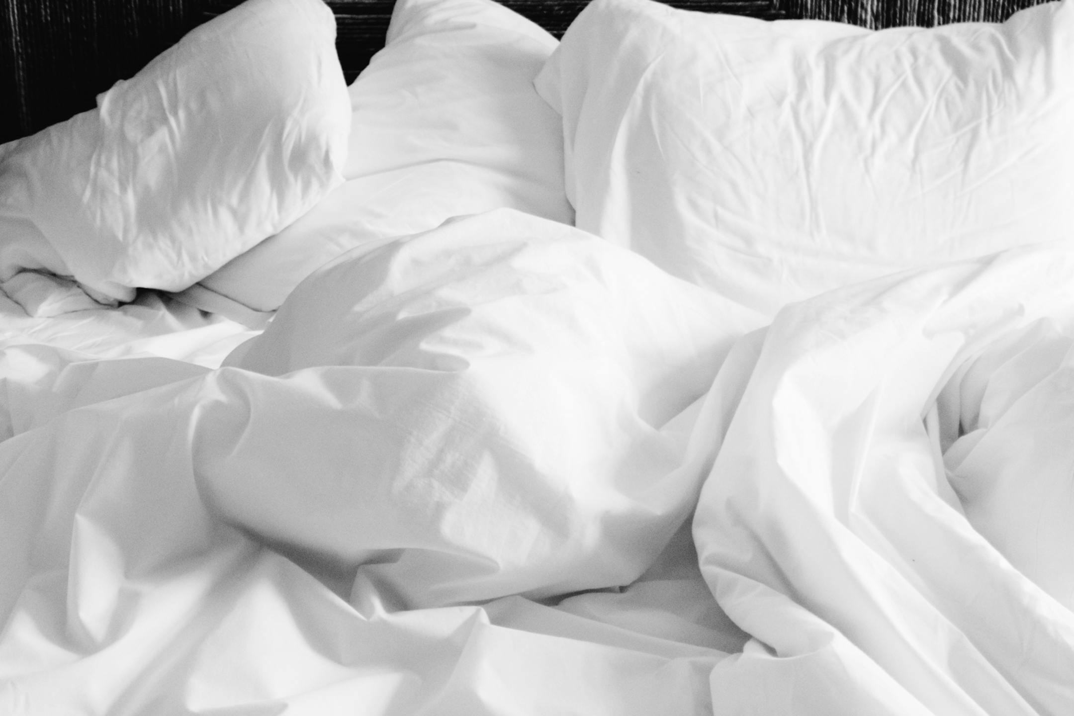 A cozy, rumpled white bed with soft sheets and pillows in a modern bedroom setting.