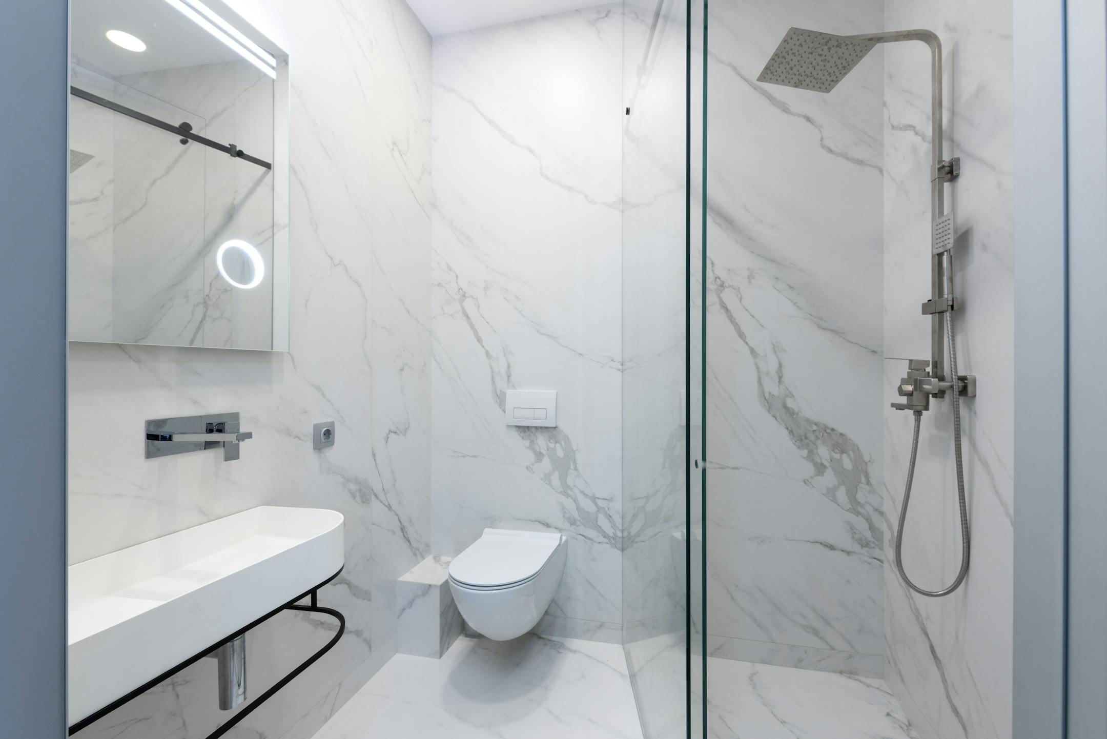 Elegant white marble bathroom featuring a sleek shower, toilet, and sink.