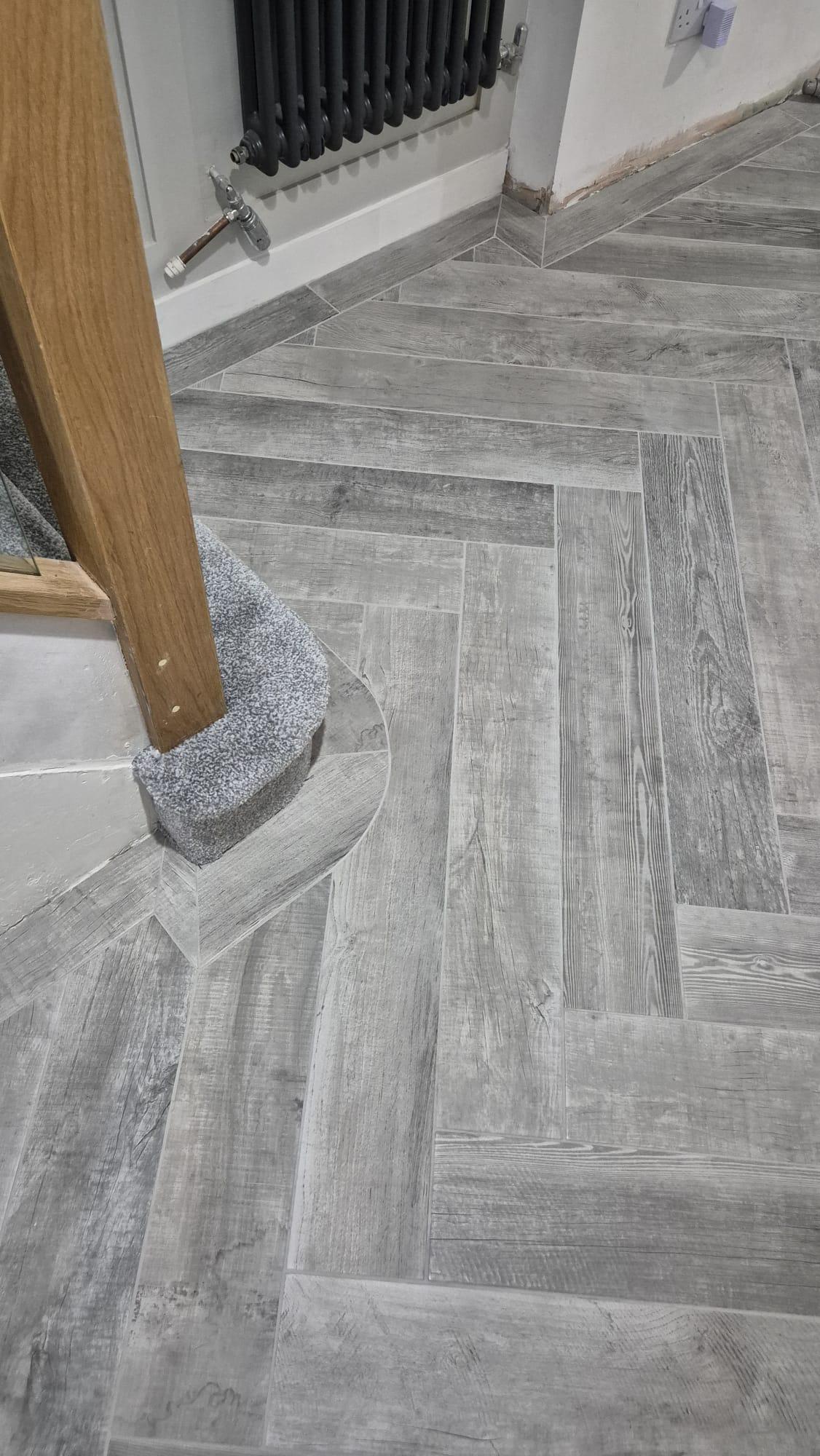 Grey herringbone wood-effect tile flooring near stair post, tiled by Coventry Tiling