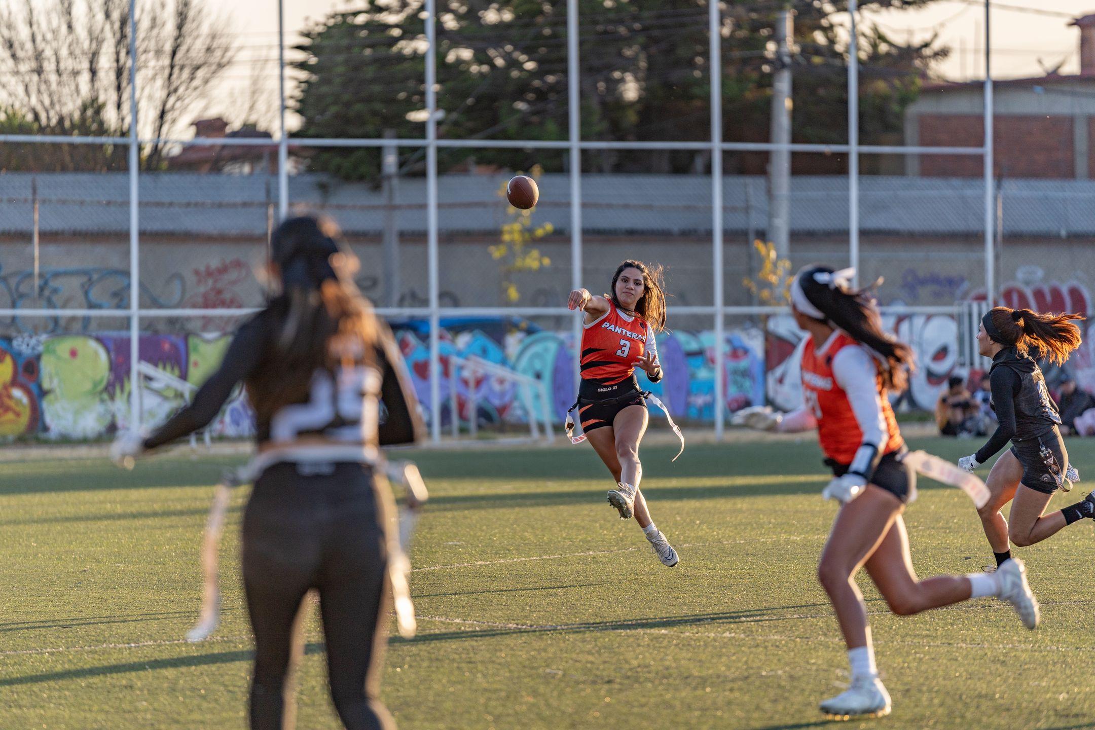 Action shot of women playing flag football on a sunny day outdoors.