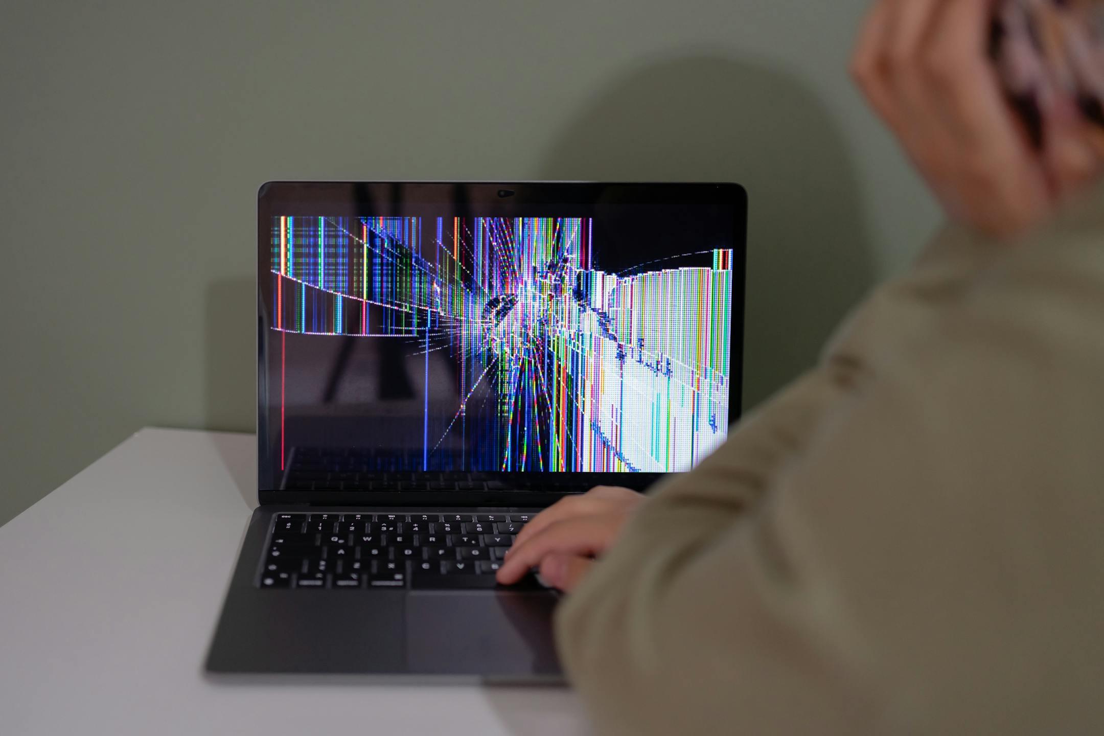 Individual viewing a laptop displaying a cracked and colorful digital screen indoors.