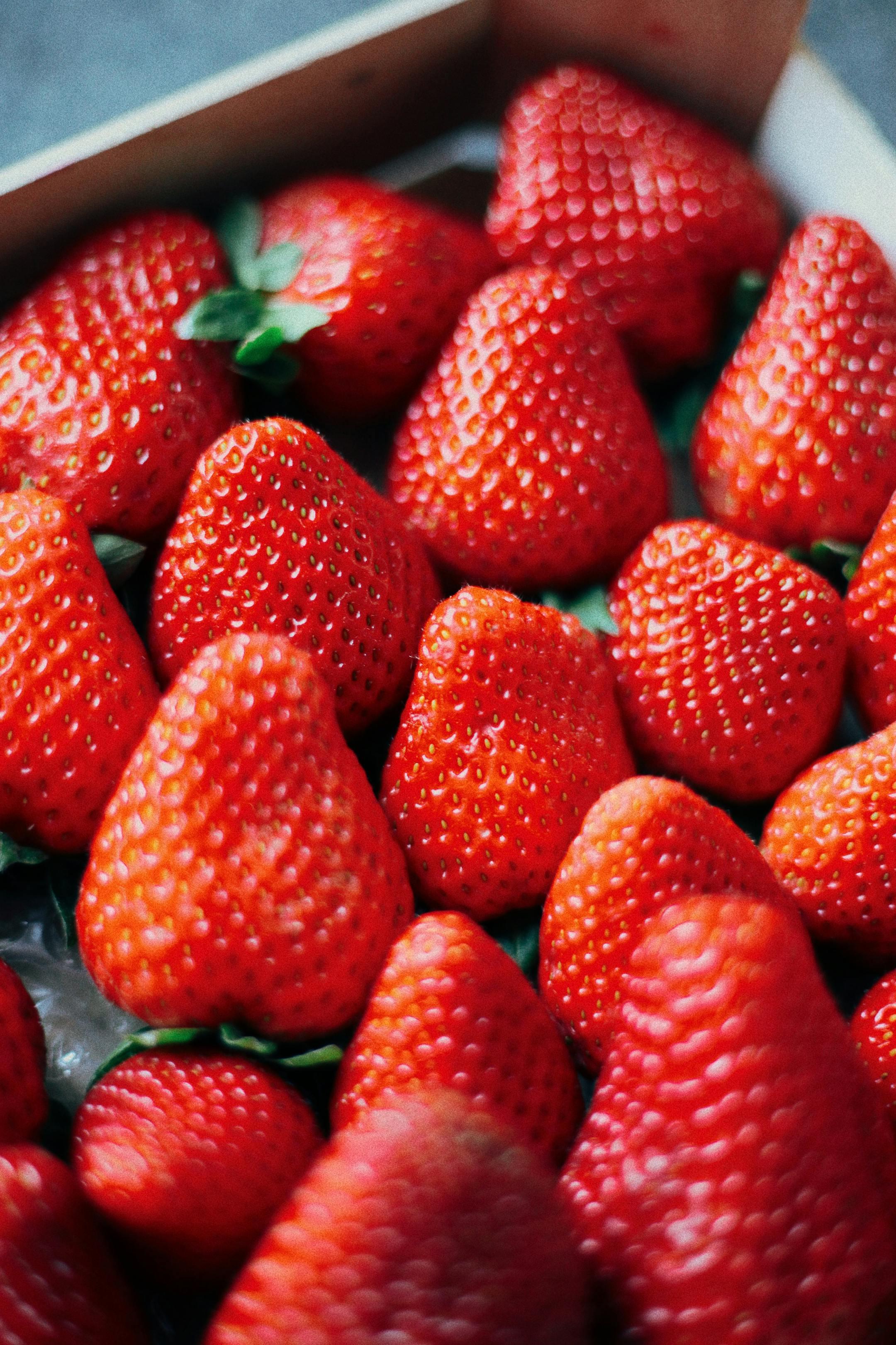Close-up of fresh ripe strawberries in a box, showcasing vibrant red color and texture.