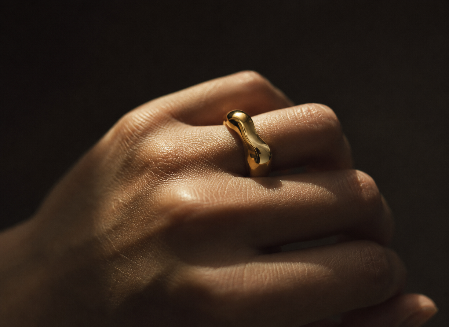 Black and white editorial — hand wearing sculptural gold ring