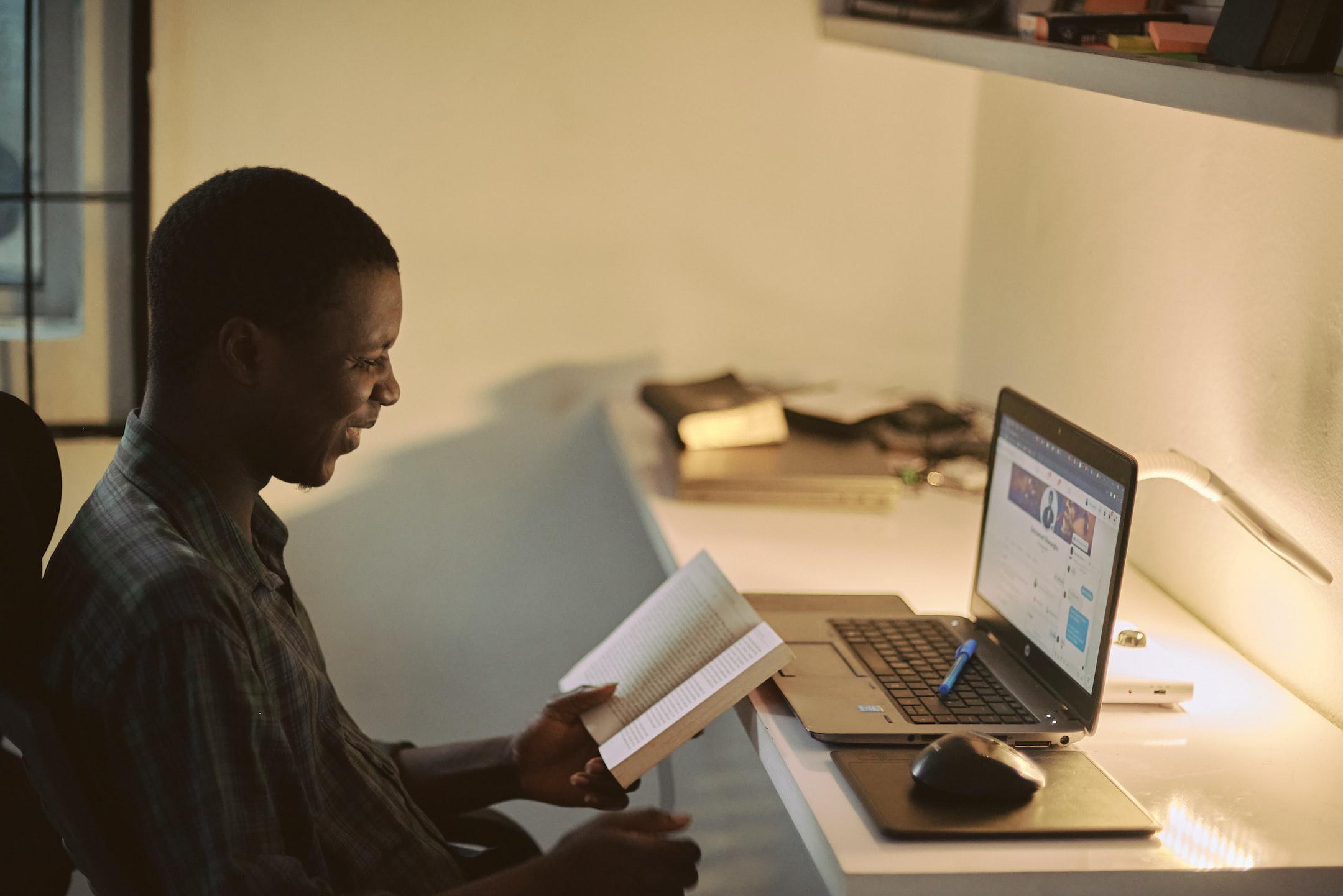 Portrait of a creative happy African man taking a break from work to enjoy reading a book, his workspace blurred in the background
