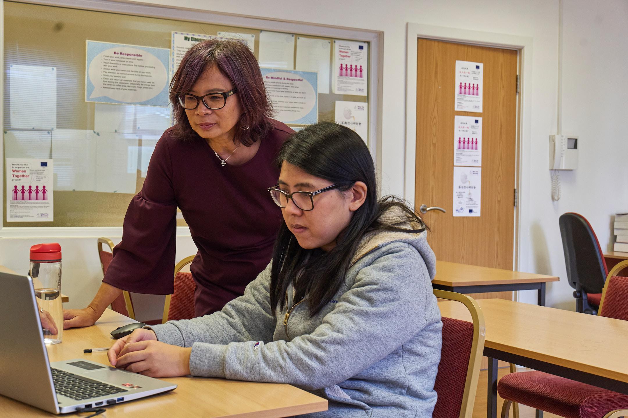 Two women working together, both are looking at the laptop screen.