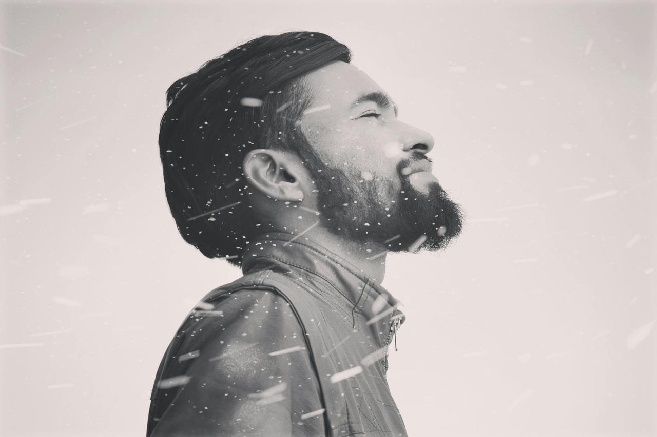 Grayscale portrait of a man meditating with a peaceful expression amidst falling snow.