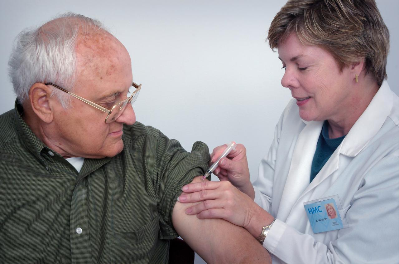 In this 2006 image, a qualified healthcare practitioner was in the process of administering an intramuscular immunization to a middle-aged man, using the man’s left shoulder muscle as the injection site. The physician immobilized the injection area with her free hand.