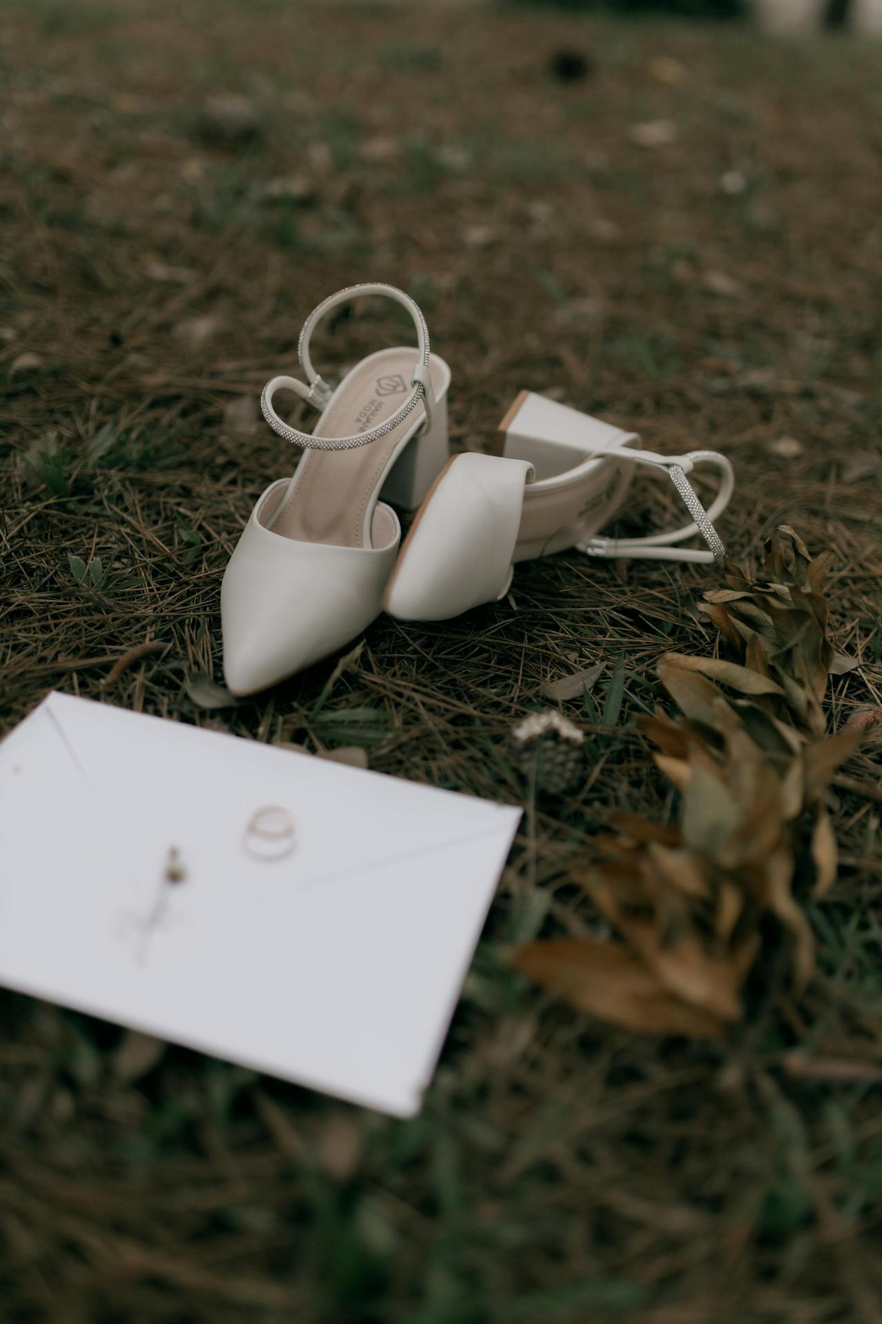 Close-up of white wedding shoes and invitation on grass, evoking romance.