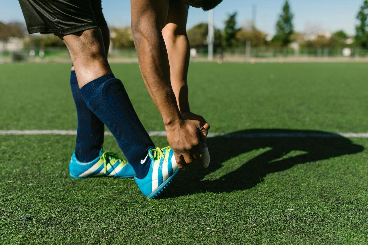 Athlete preparing with stretches on a green soccer field during a sunny day.