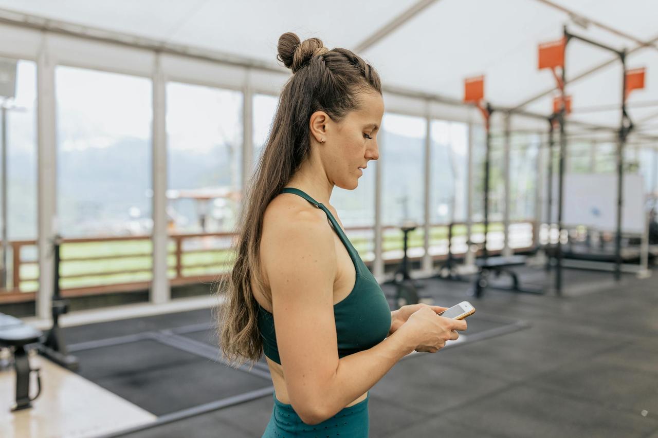 Female athlete in gym looking at phone, dressed in activewear for training.