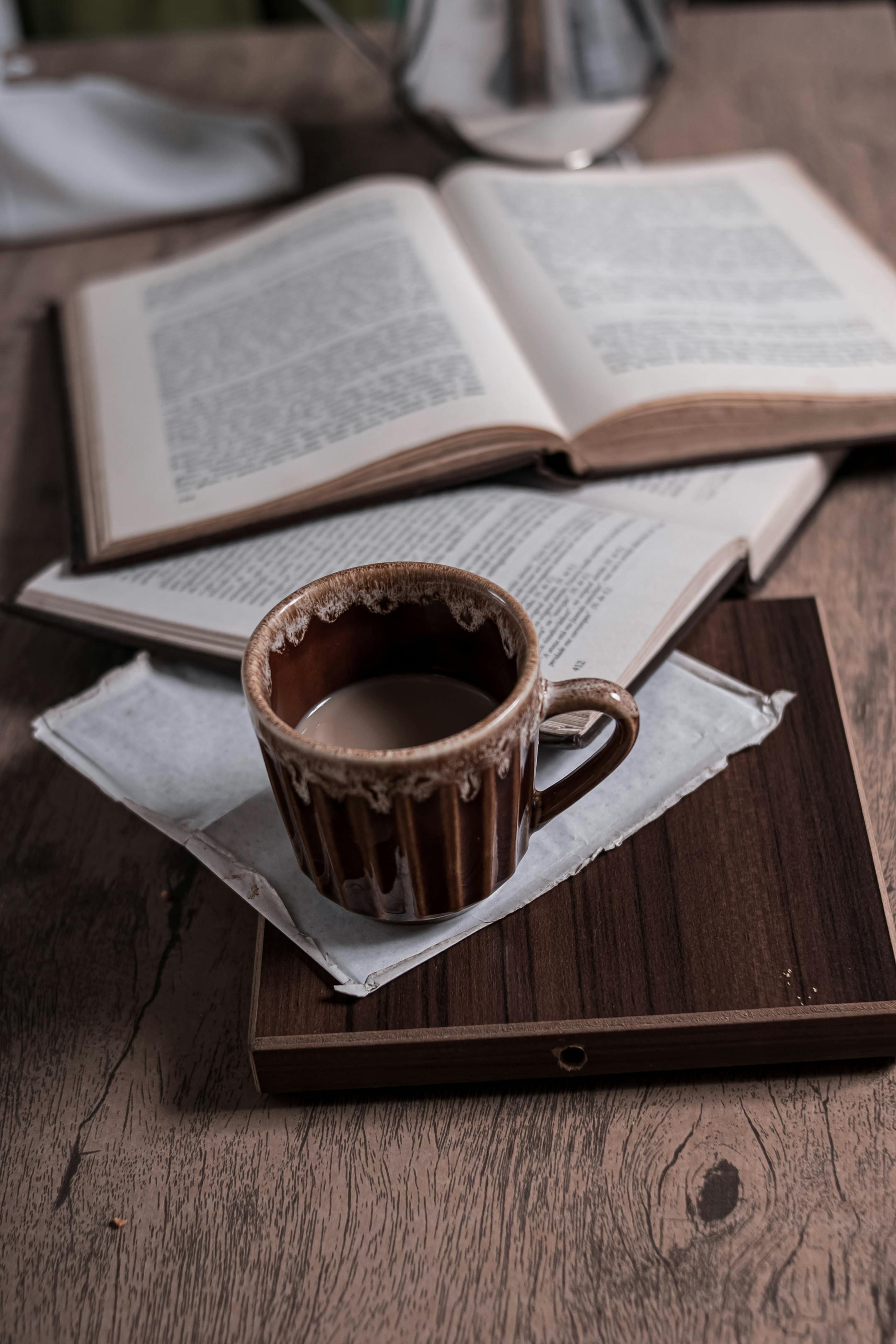 Brown coffee cup with open books on a rustic wooden table, perfect for a cozy atmosphere.