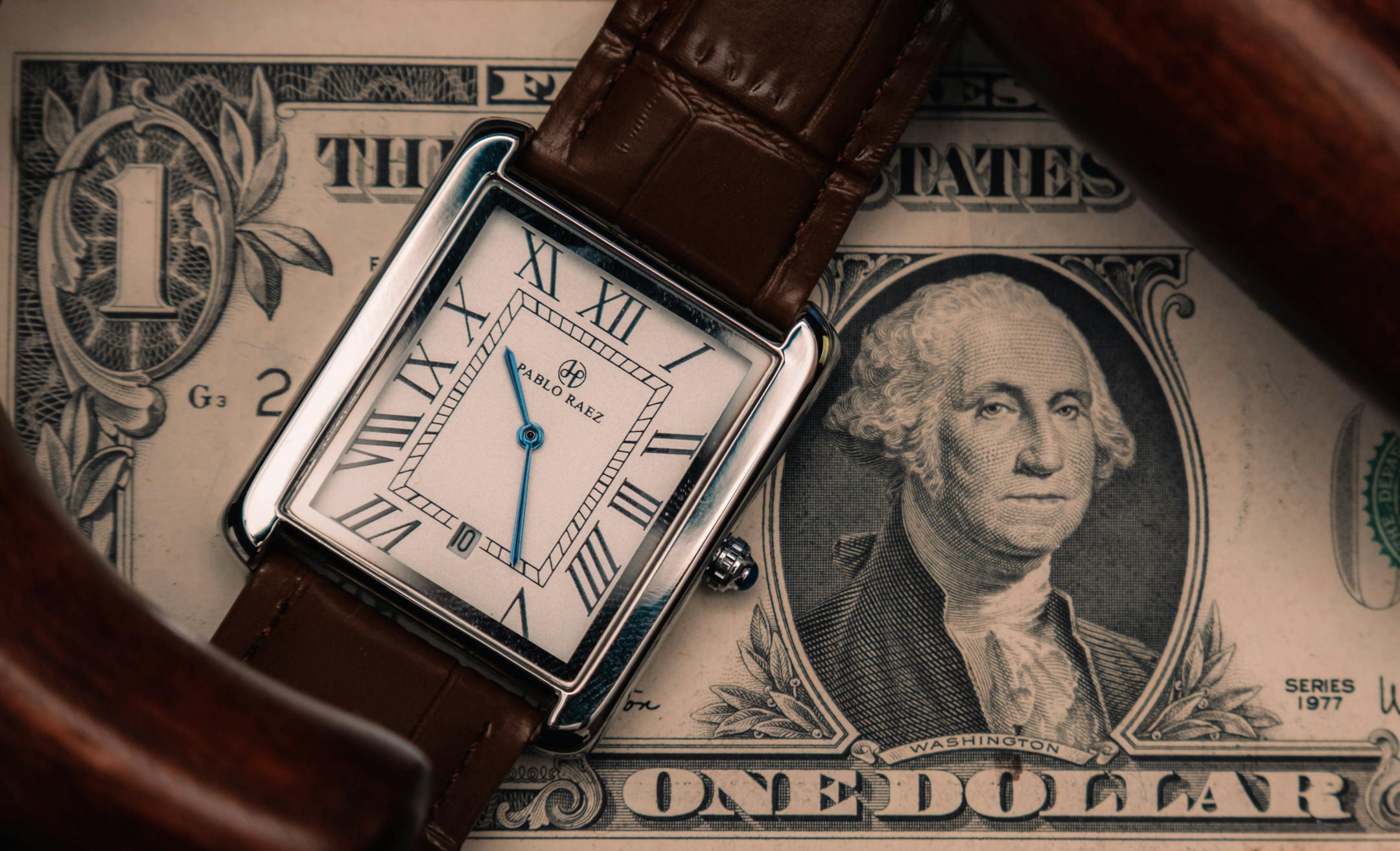 A classic watch placed on a US dollar bill, symbolizing time and money.
