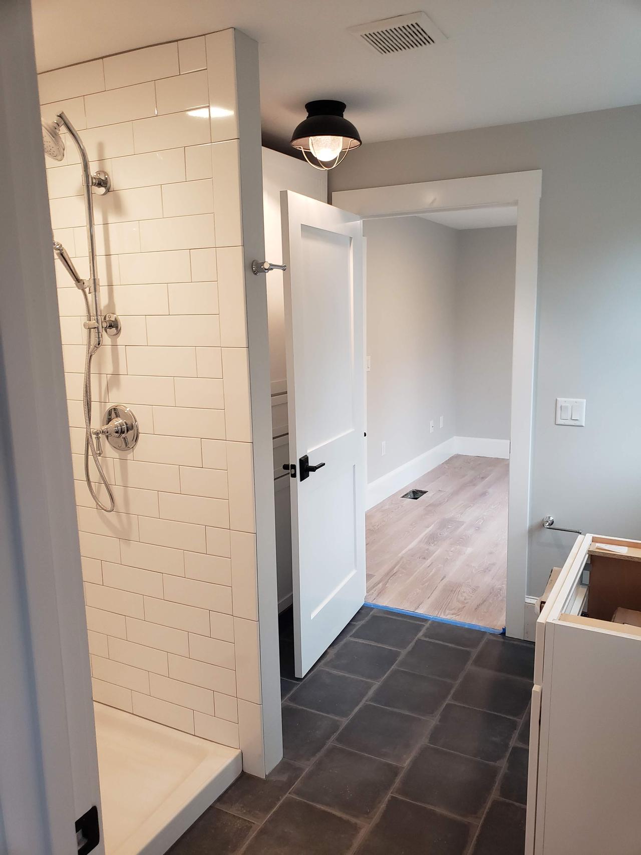 door-open-to-small-bathroom-with-white-tiled-shower-and-grey-stone-floor-tile