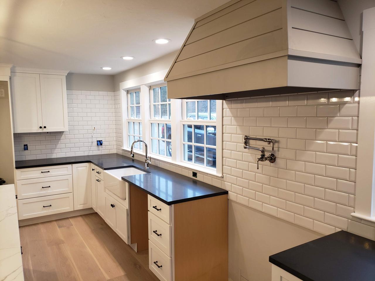 refinished-white-kitchen-cabinets-with-white subway-tiles-sink-three-windows-and-large-stove-hood