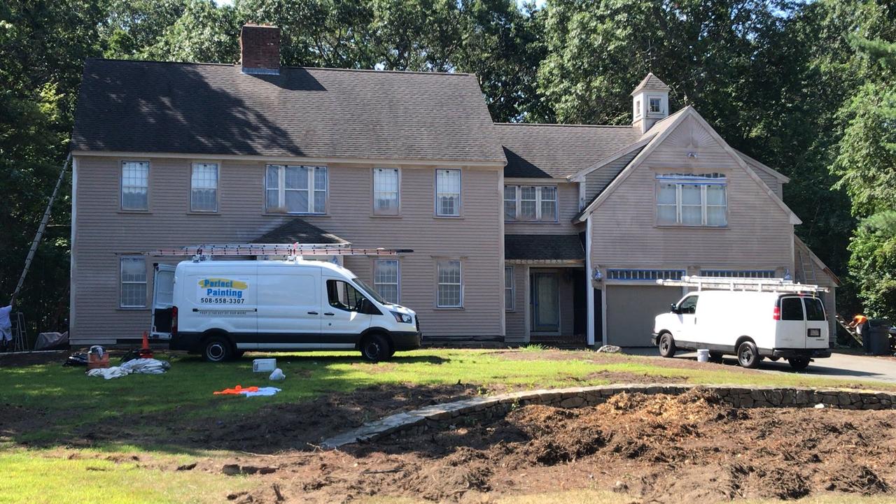 two-white-vans-with-ladders-in-front-of-large-grey-house-prepping-for-painting