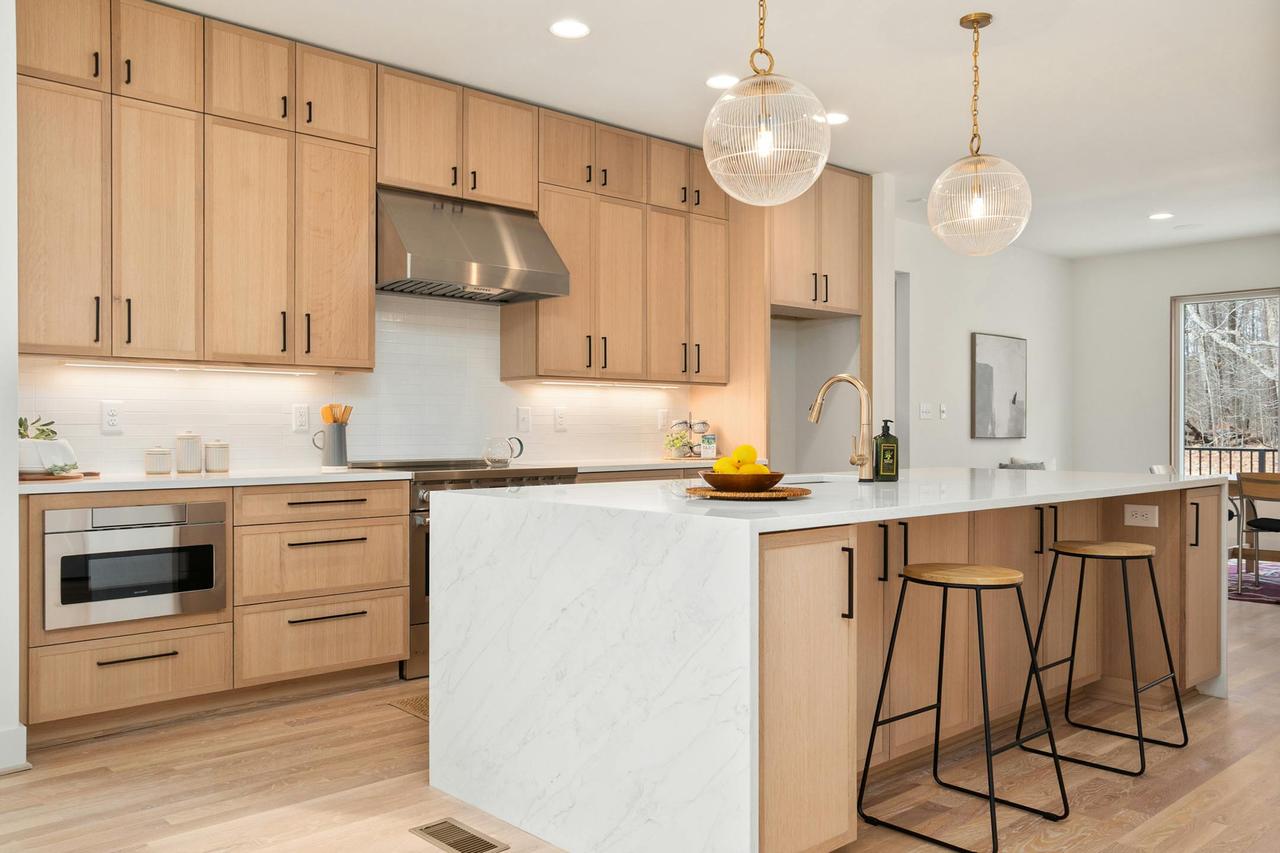 Bright modern kitchen with wood cabinets, marble island, and pendant lights, epitomizing Scandinavian design.