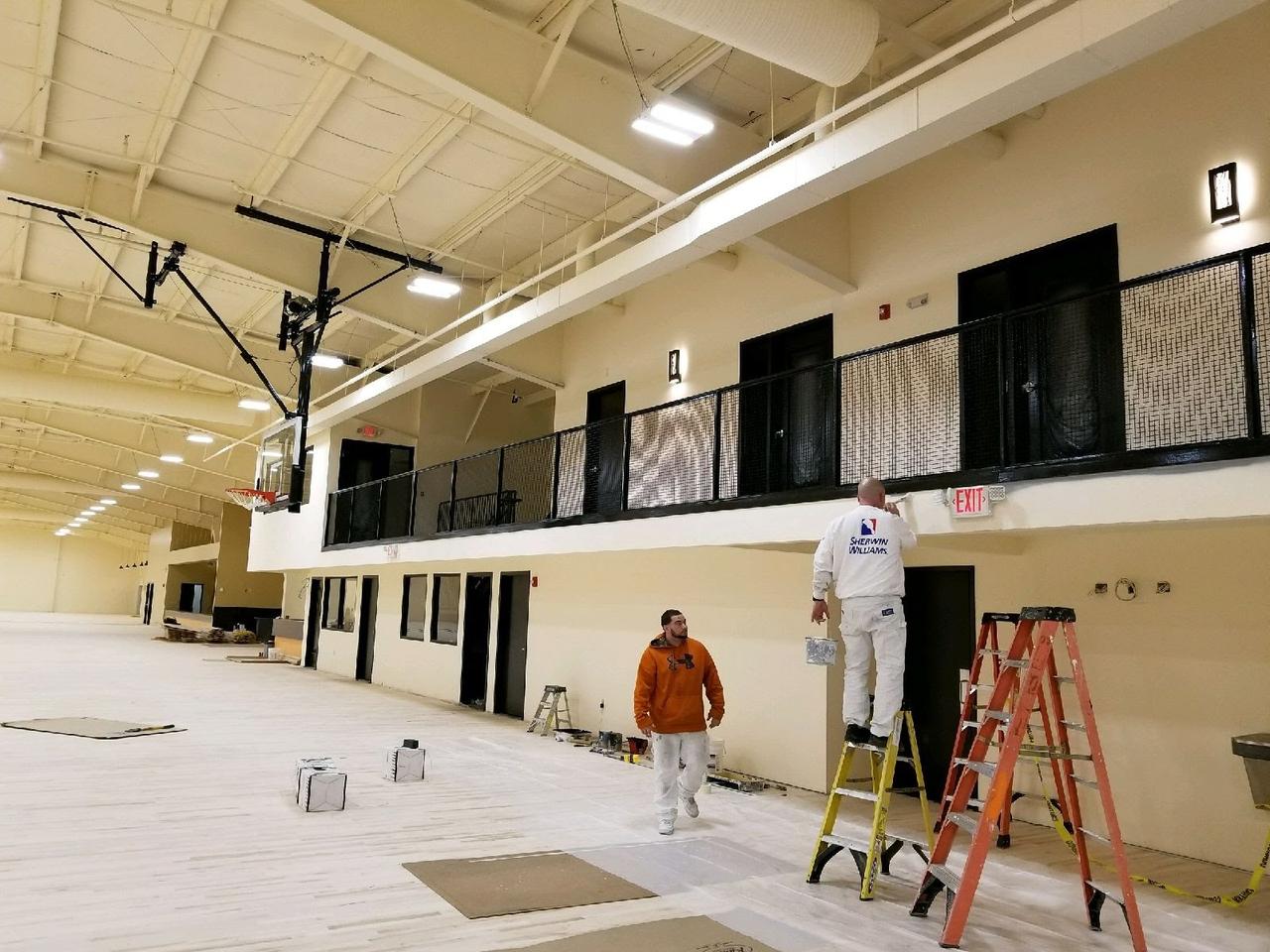 two-males-with ladders-painting-interior-upper-deck-of-basketball-court
