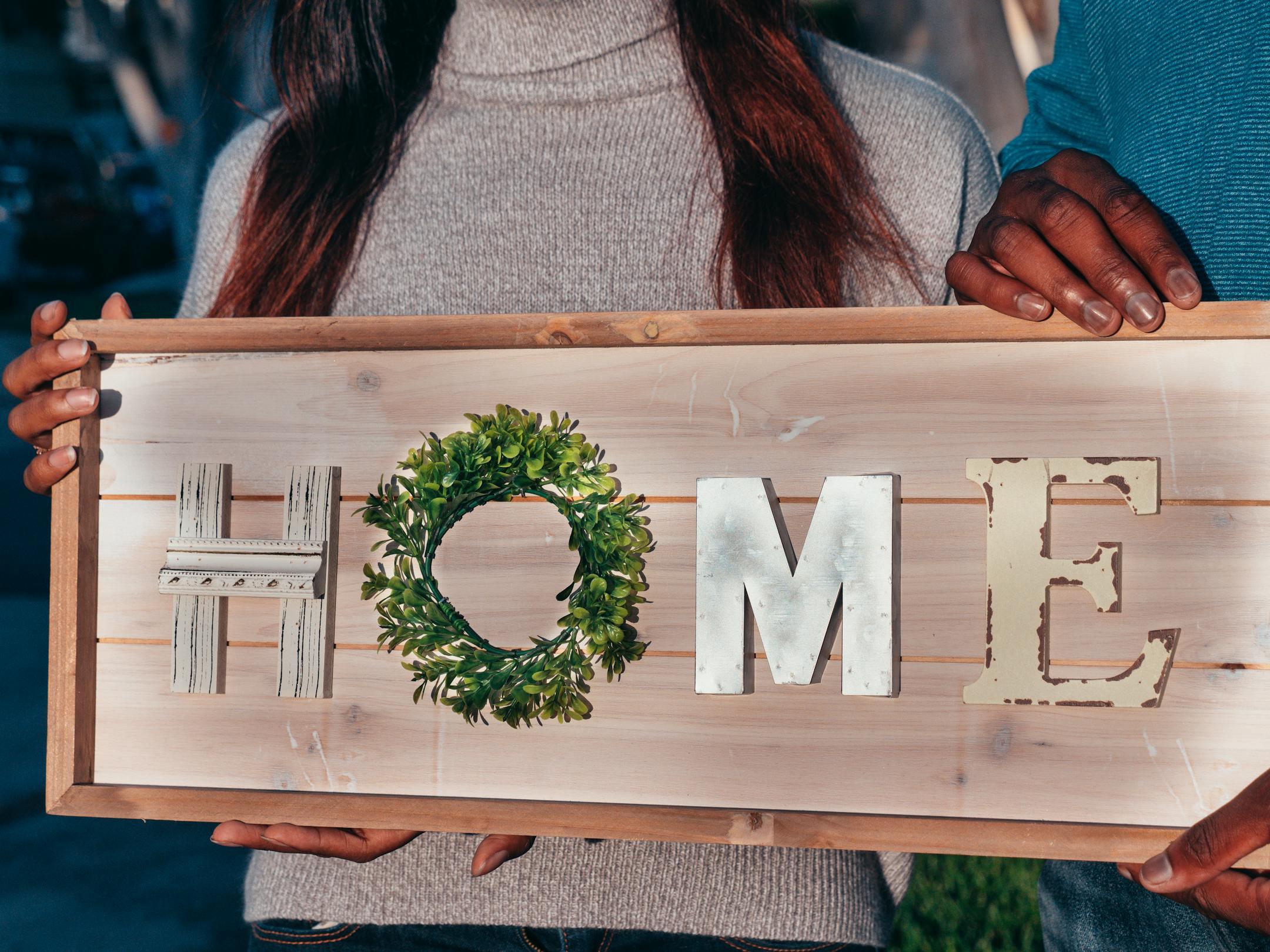 A couple holding a wooden sign spelling 'HOME' to celebrate their new residence.