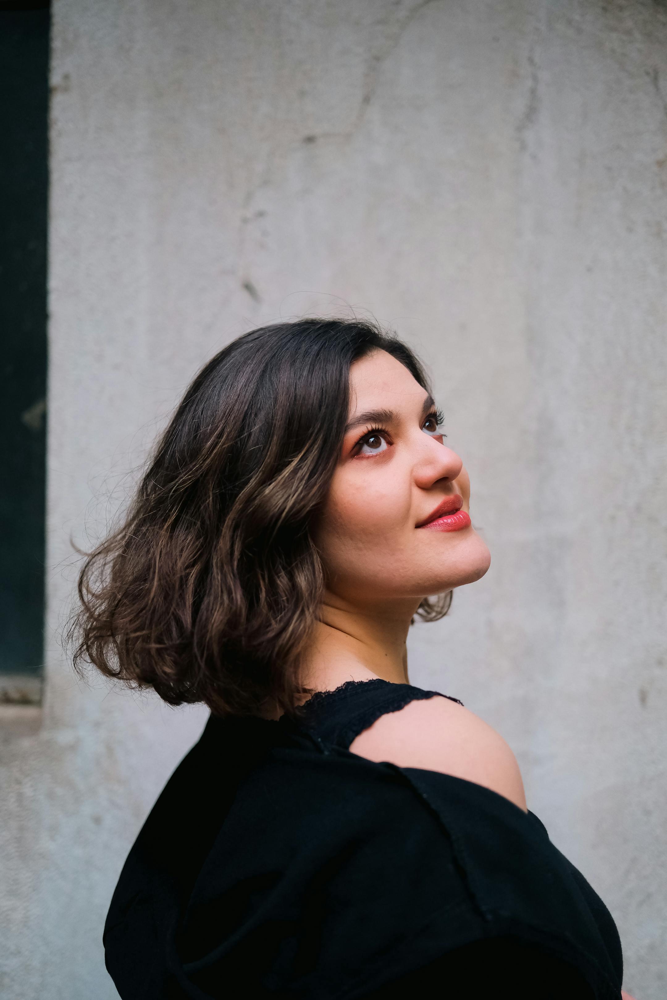A stylish young woman with short brunette hair gazes upwards in a vertical shot.