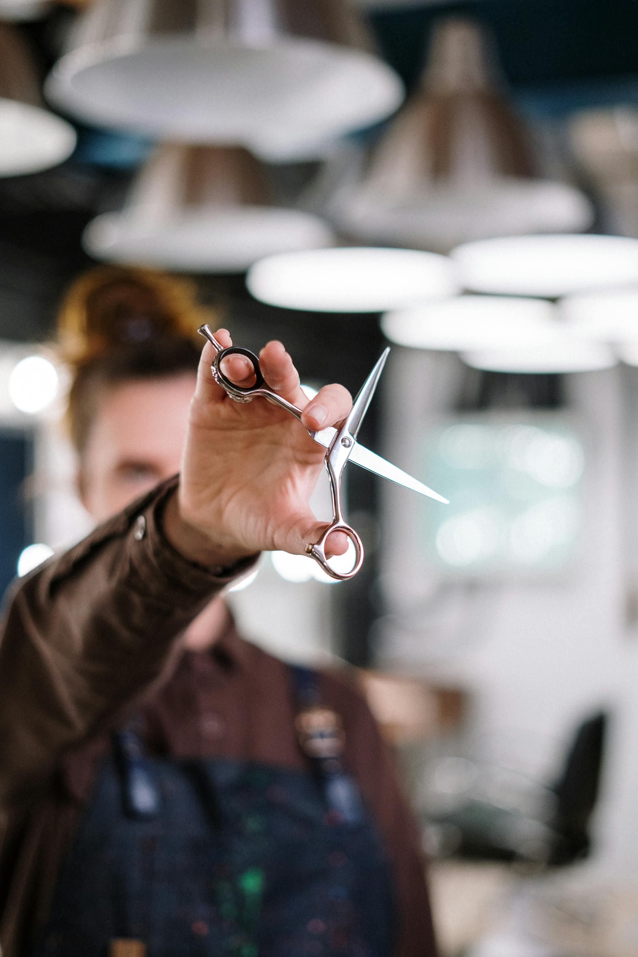 Close-up of a hairstylist holding scissors in a modern salon with blurred background.
